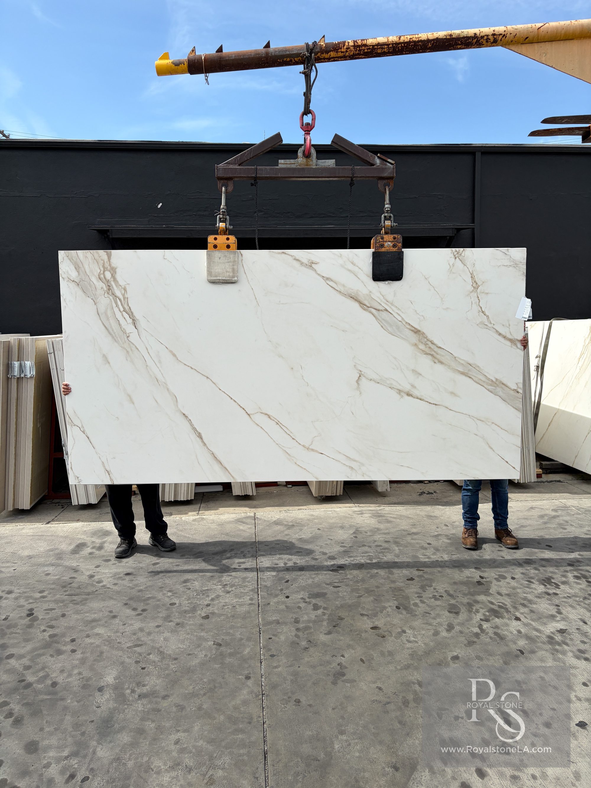 Second view of the same ABK Calacatta Gold porcelain panel on the crane, showing the diagonal gold vein network running corner to corner across the honed white ground