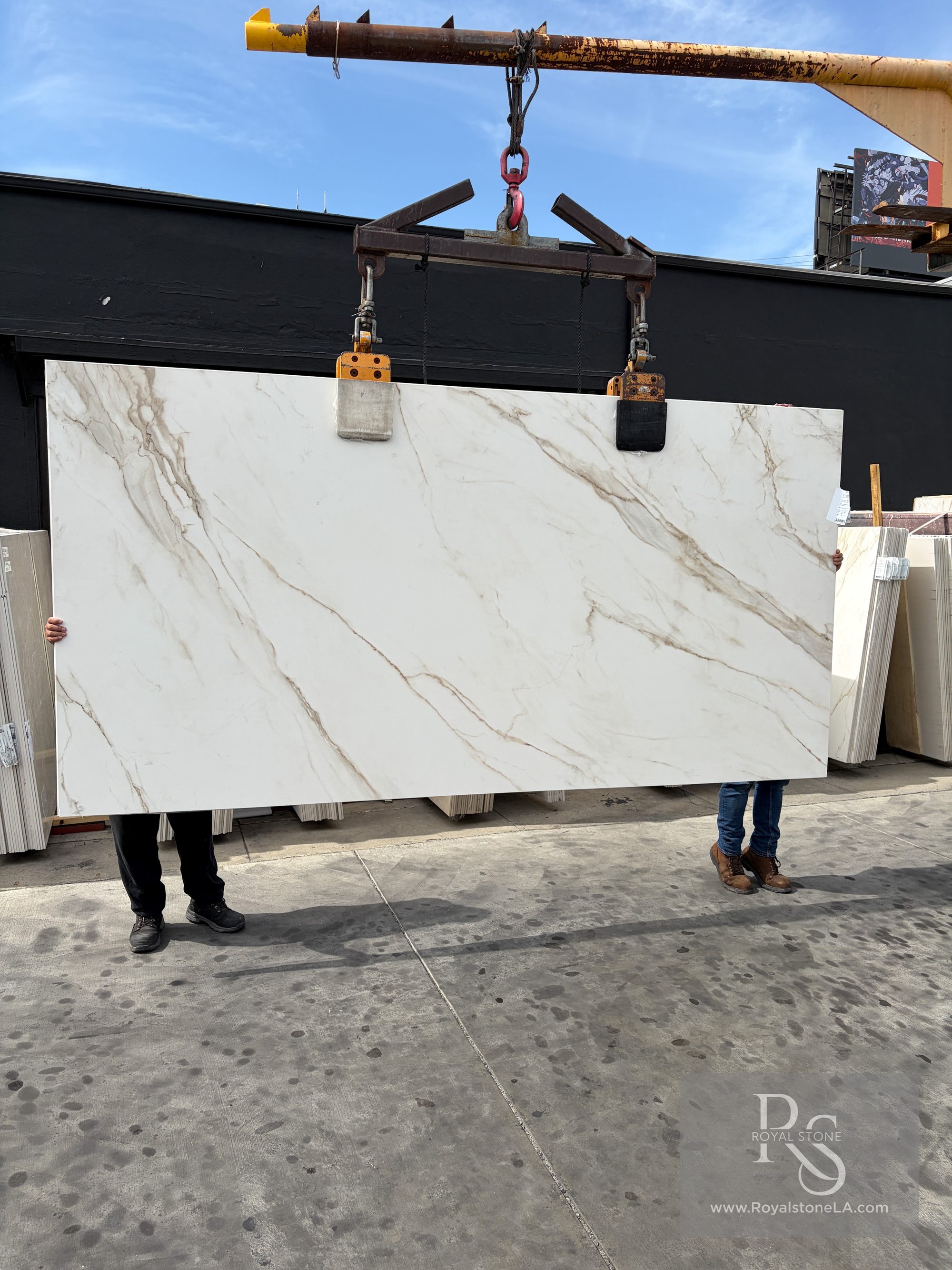 1.2cm ABK Calacatta Gold porcelain panel honed finish 63 by 126 inches lifted on a crane in the Royal Stone yard, white field with diagonal gold and warm grey veining, freshly imported from Italy