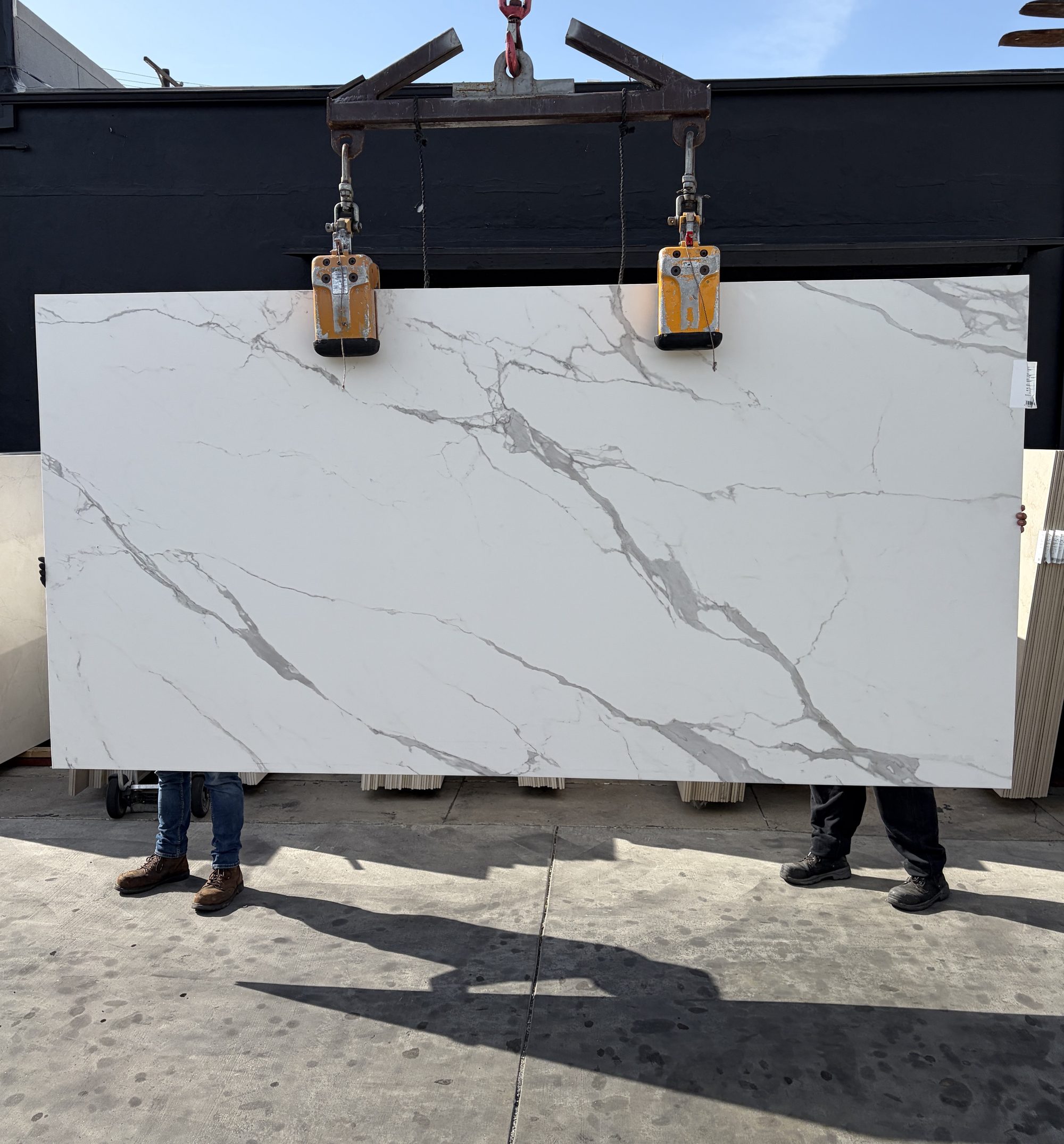 1.2cm ABK Statuario porcelain panel honed finish 63 by 126 inches lifted on a crane in the Royal Stone yard, bright cool white ground with diagonal grey veining and silvery secondary network, freshly imported from Italy
