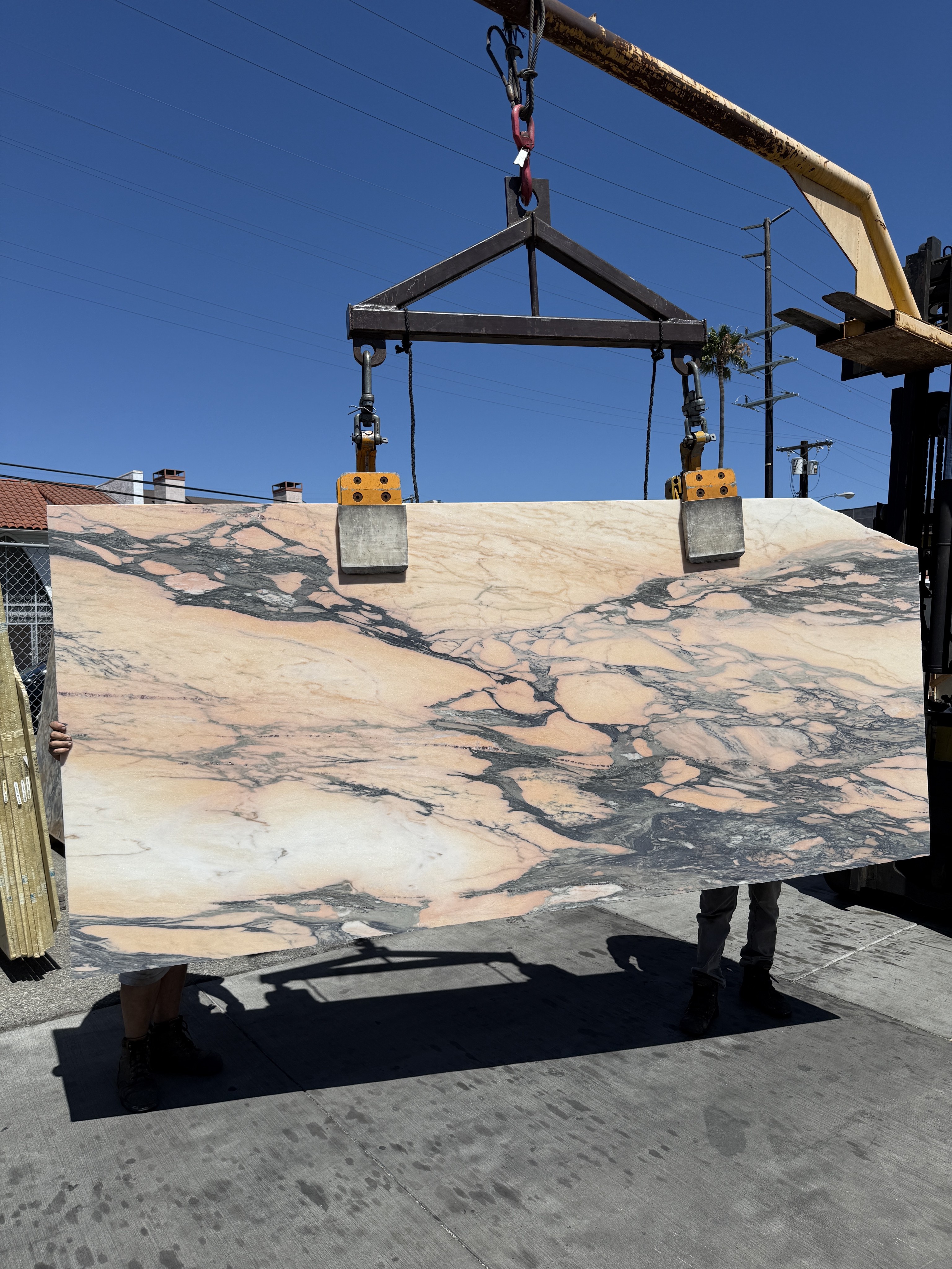 Antolini Calacatta Viola Rosenoir Paonazzo marble slab DX488 honed on the crane against blue sky, peach and rose field with dramatic storm-grey and black veining