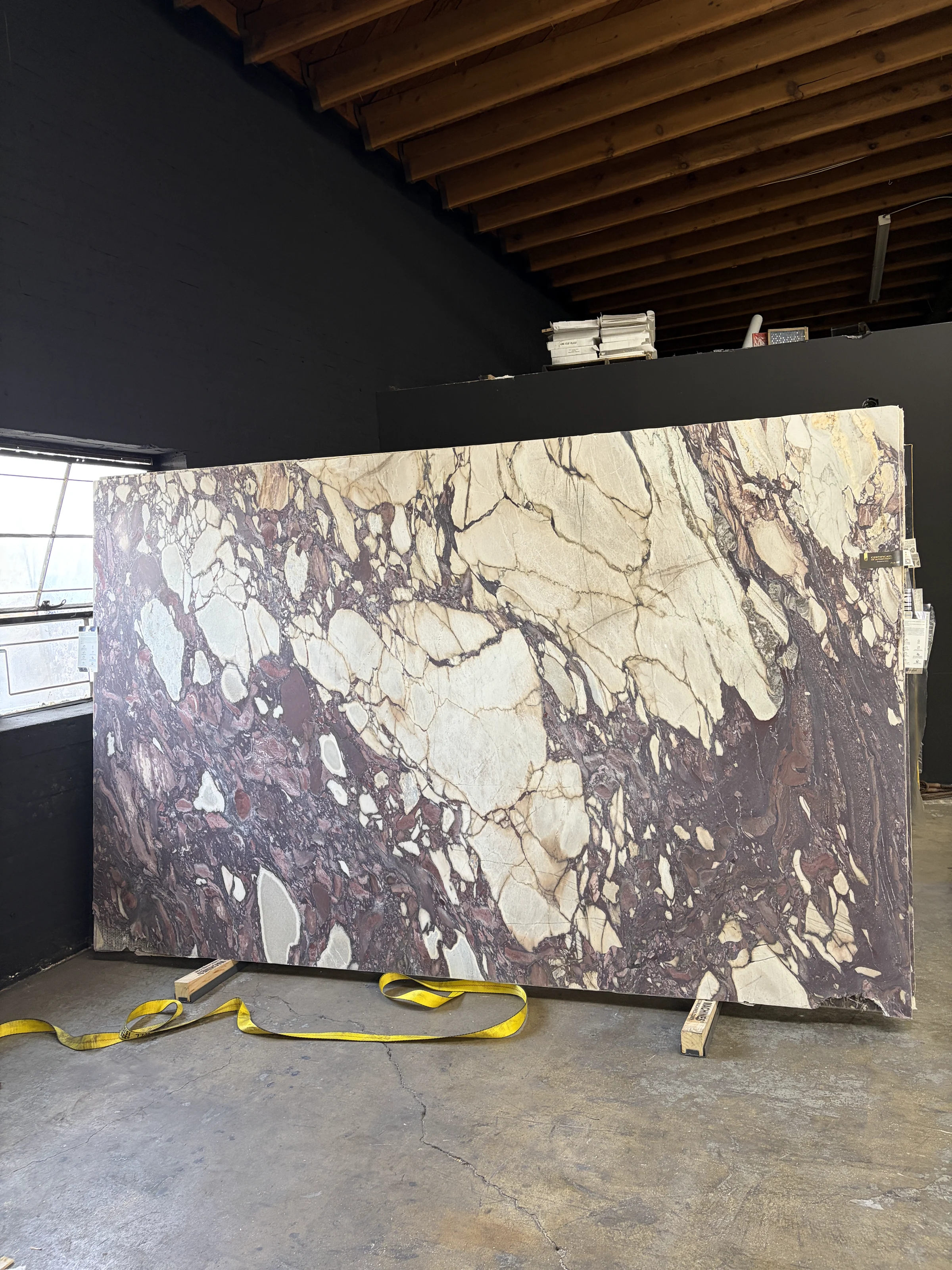 Antolini Calacatta Viola Top EE693 honed marble slab from the same lot at Royal Stone, showing its full plum, violet, cream, and charcoal brecciated movement in the indoor yard