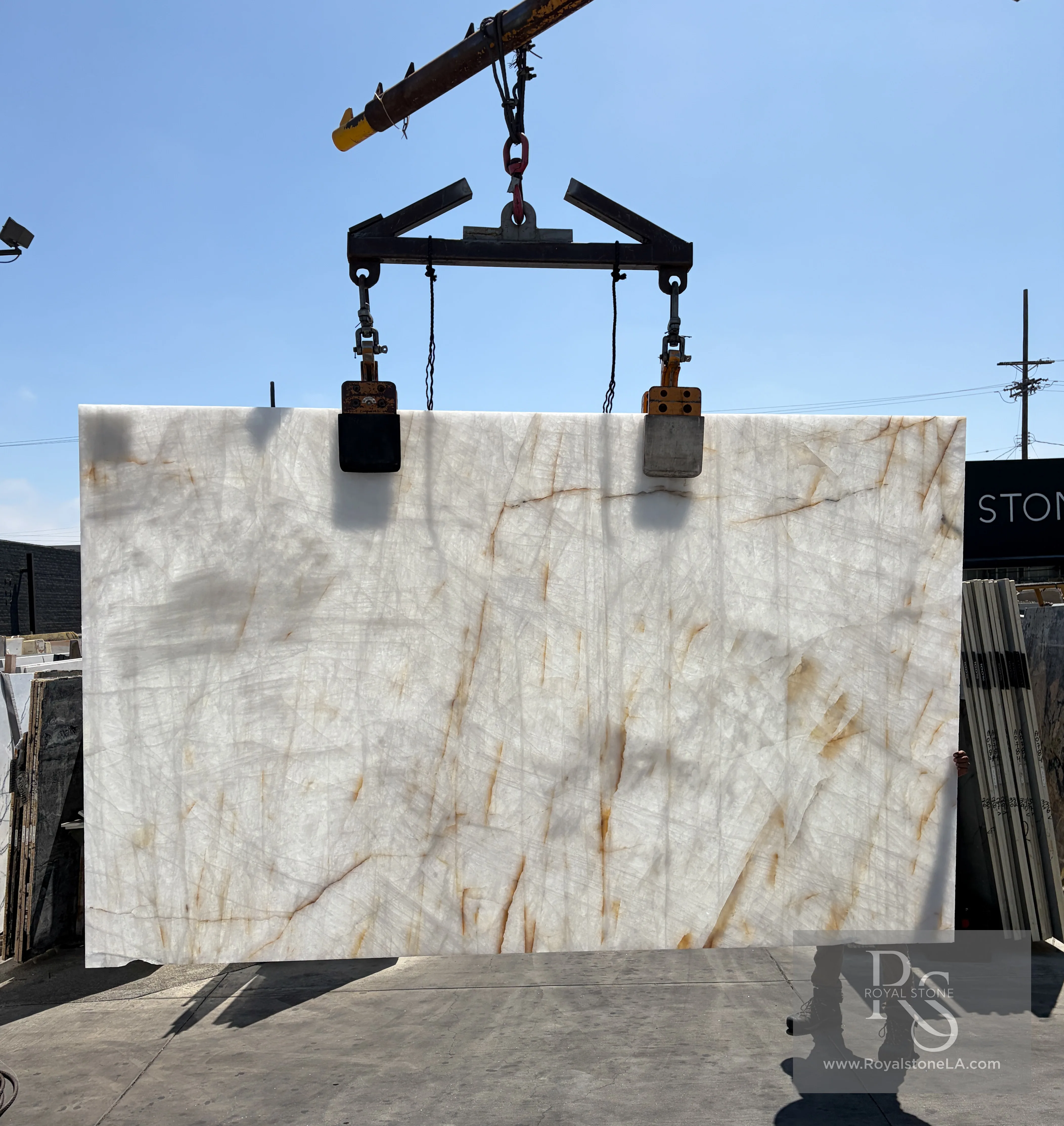 2cm Antolini Cristallo ED867 Lumix quartzite slab, leather finish, 76 by 125 inches — backlit, the translucent white field glowing and the warm gold filaments lit through the stone at the Royal Stone yard