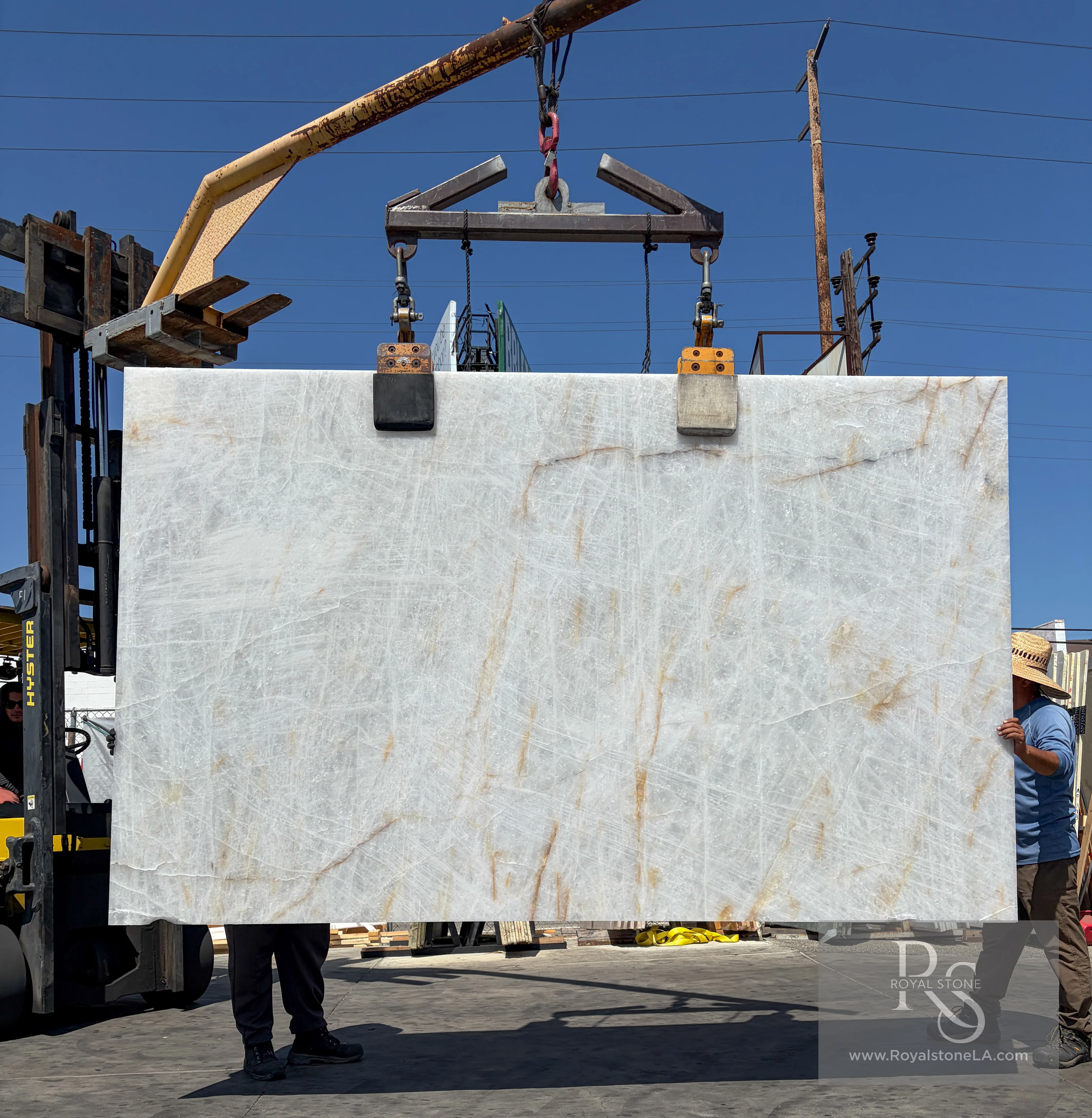 2cm Antolini Cristallo ED867 Lumix quartzite slab, leather finish, 76 by 125 inches — translucent white field with warm gold filament veining, lifted by crane at the Royal Stone Los Angeles yard in daylight