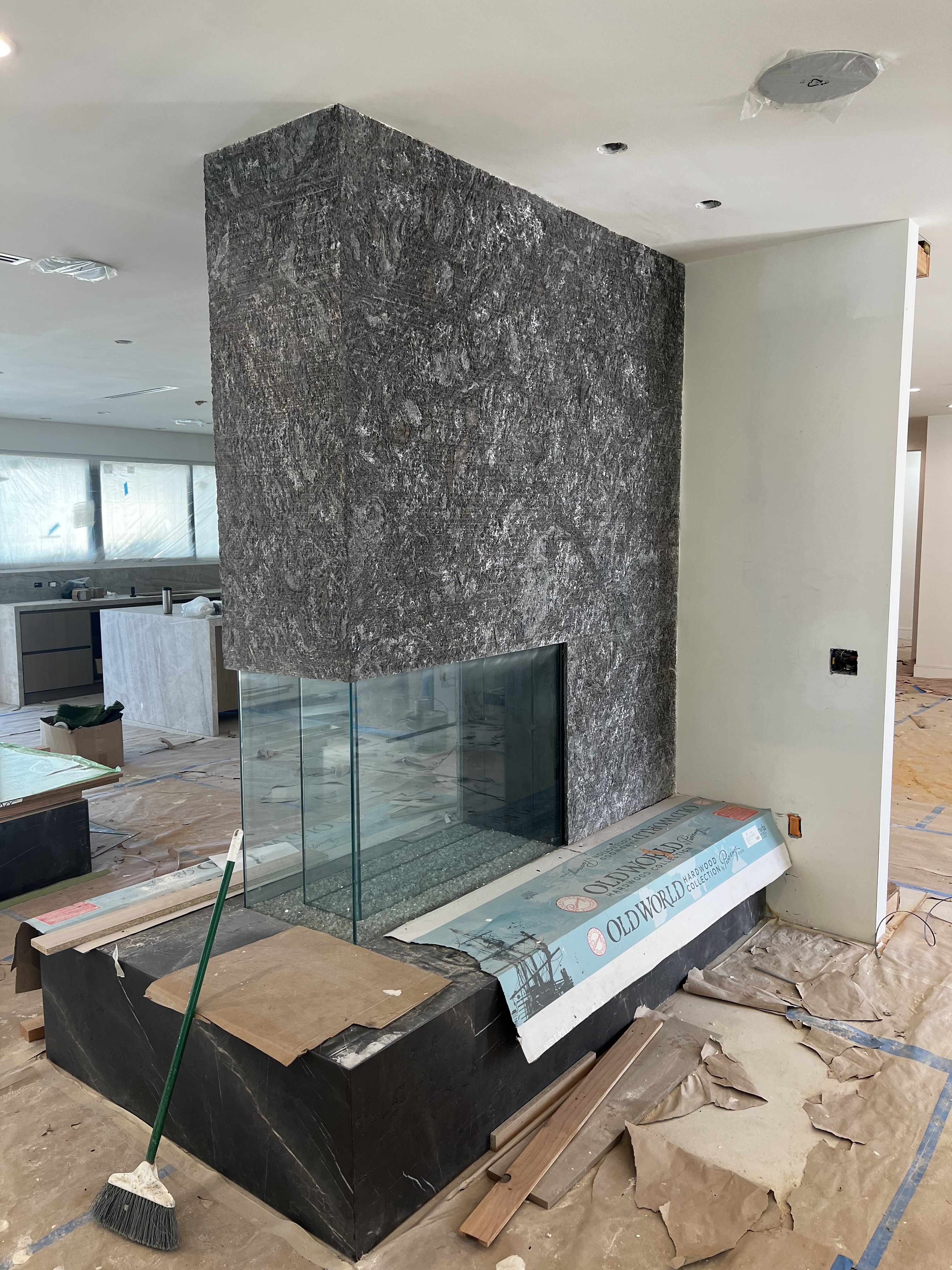 Antolini Kosmos Quartzite Super Cleft Texture installed as a freestanding double-sided fireplace mass with a full-height glass firebox and a honed black soapstone hearth and base, in a Westside primary living room in finish stage