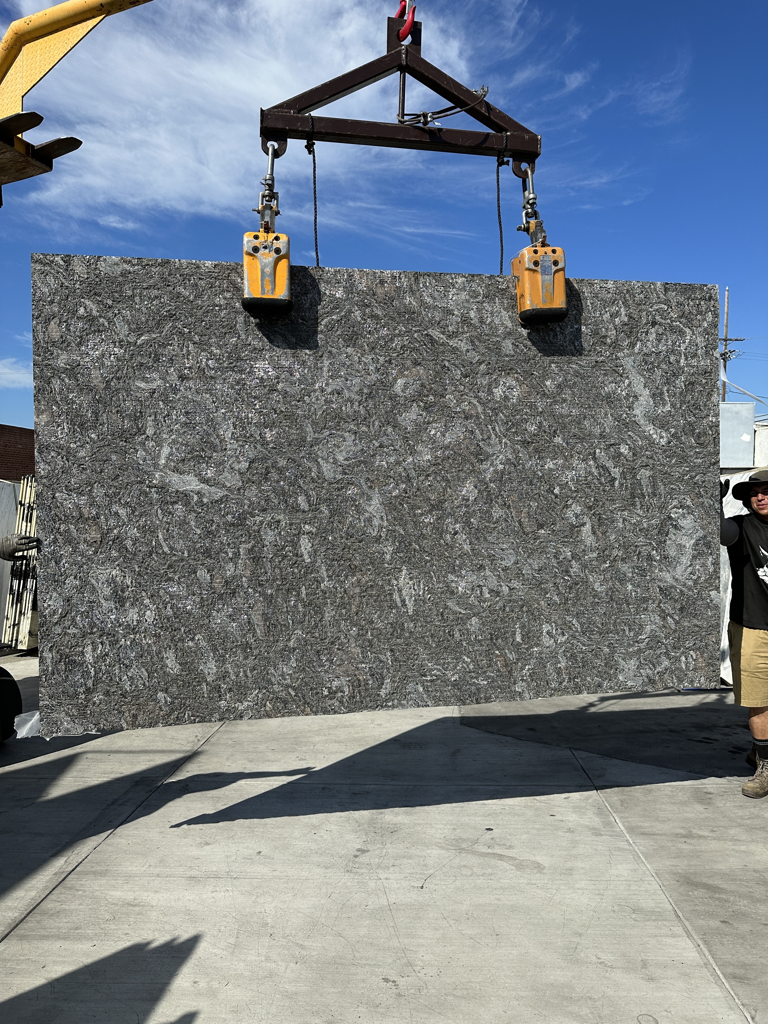 Antolini Kosmos Quartzite slab Super Cleft Texture finish on a crane in the Royal Stone yard, charcoal grey ground with silver mica, paler swirled veining and rust passages, 129 by 74 inches