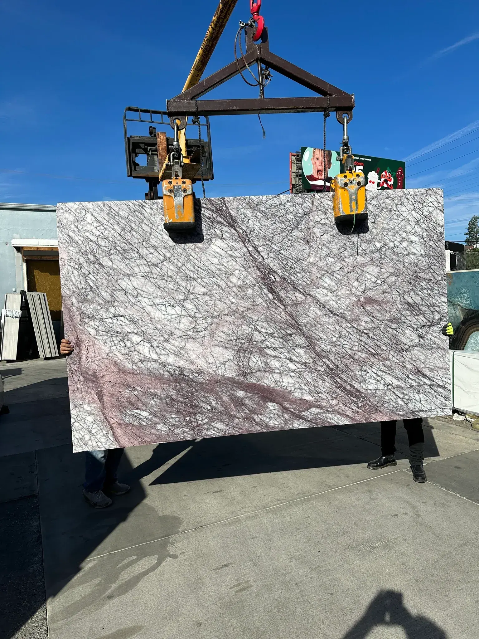Antolini Lilac Viola Premium Extra Select marble slab, 103 by 63 inches, polished finish, dusty rose and lilac field webbed with a dense net of fine plum and near-black veining with pockets of brighter pink and white quartz, lifted by crane under blue sky at Royal Stone in Los Angeles