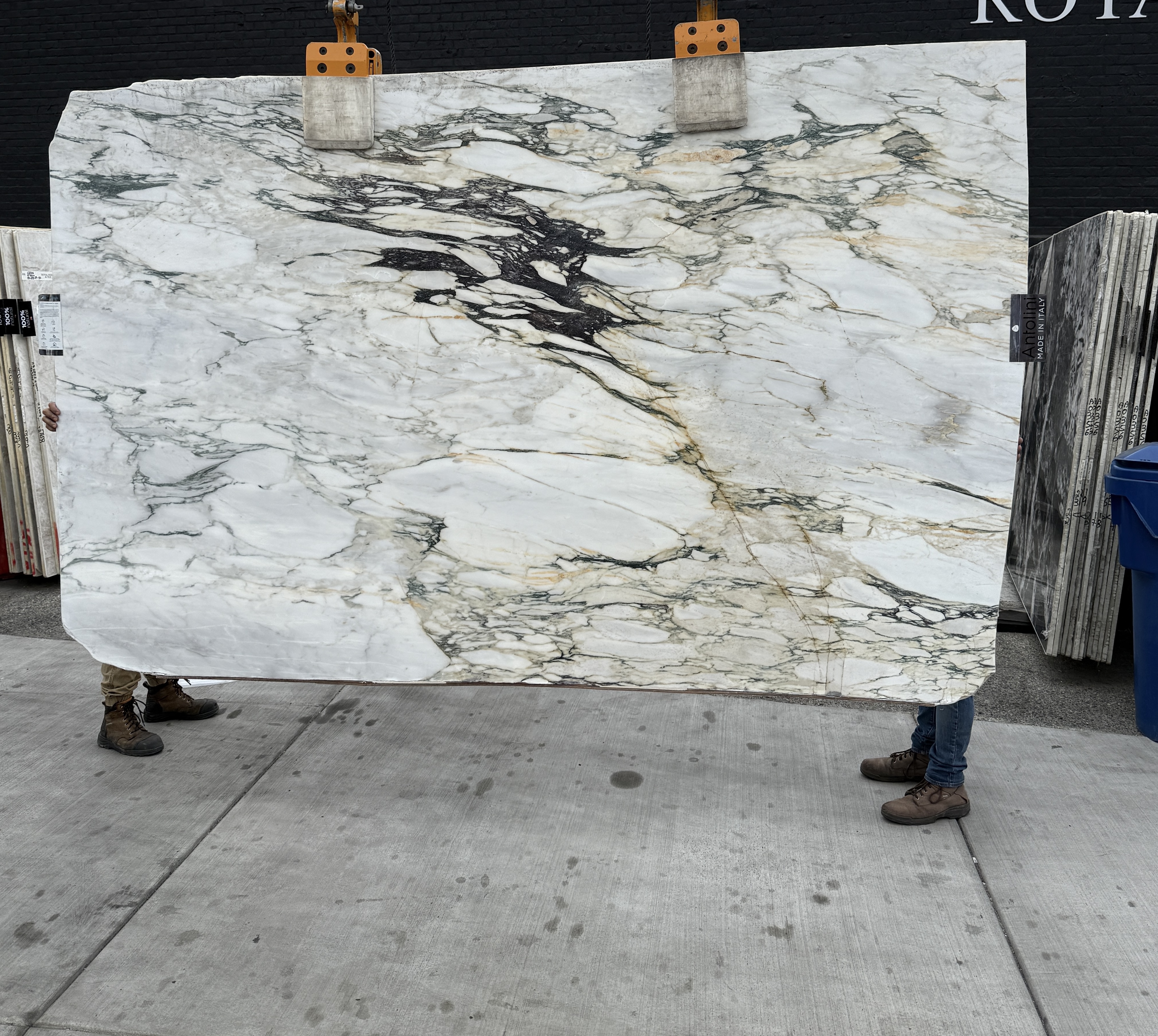 Antolini Monet Viola Classic marble slab YG373 polished at 76 by 119 inches lifted on the crane at Royal Stone Los Angeles, chalk-white field with sage-green and gold veining and a dramatic black ink-splash inclusion