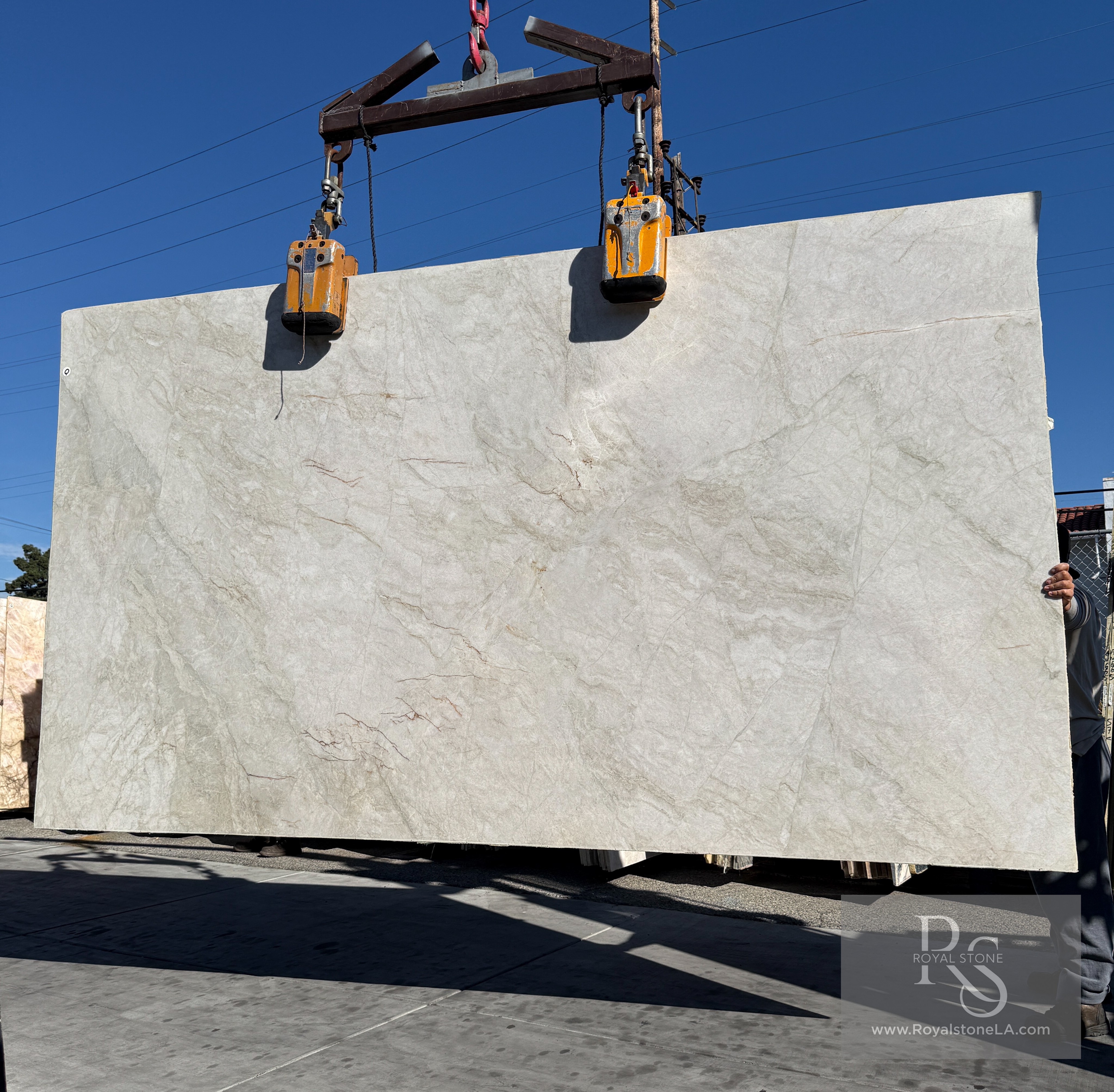 Antolini Taj Mahal quartzite commercial grade honed slab 78 by 137 inches lifted on the crane against blue sky, warm ivory field with soft taupe movement
