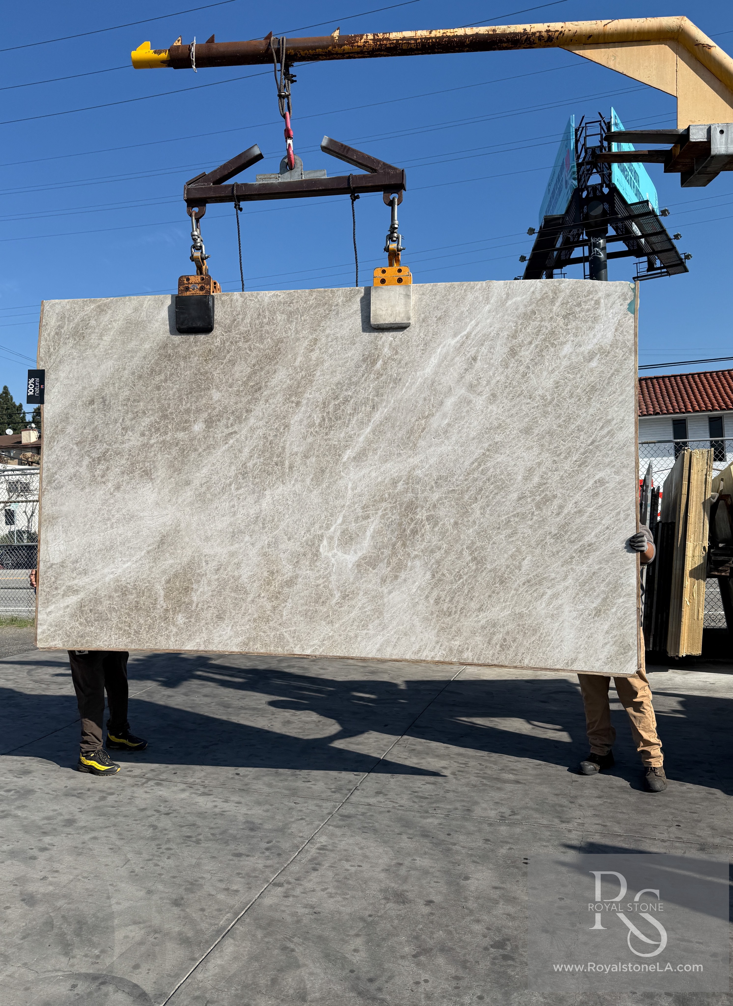 Antolini Taj Mahal Naica quartzite slab AO792 in heavy leather finish lifted on the crane against blue sky, cool pearl-grey field with fine crystalline veining