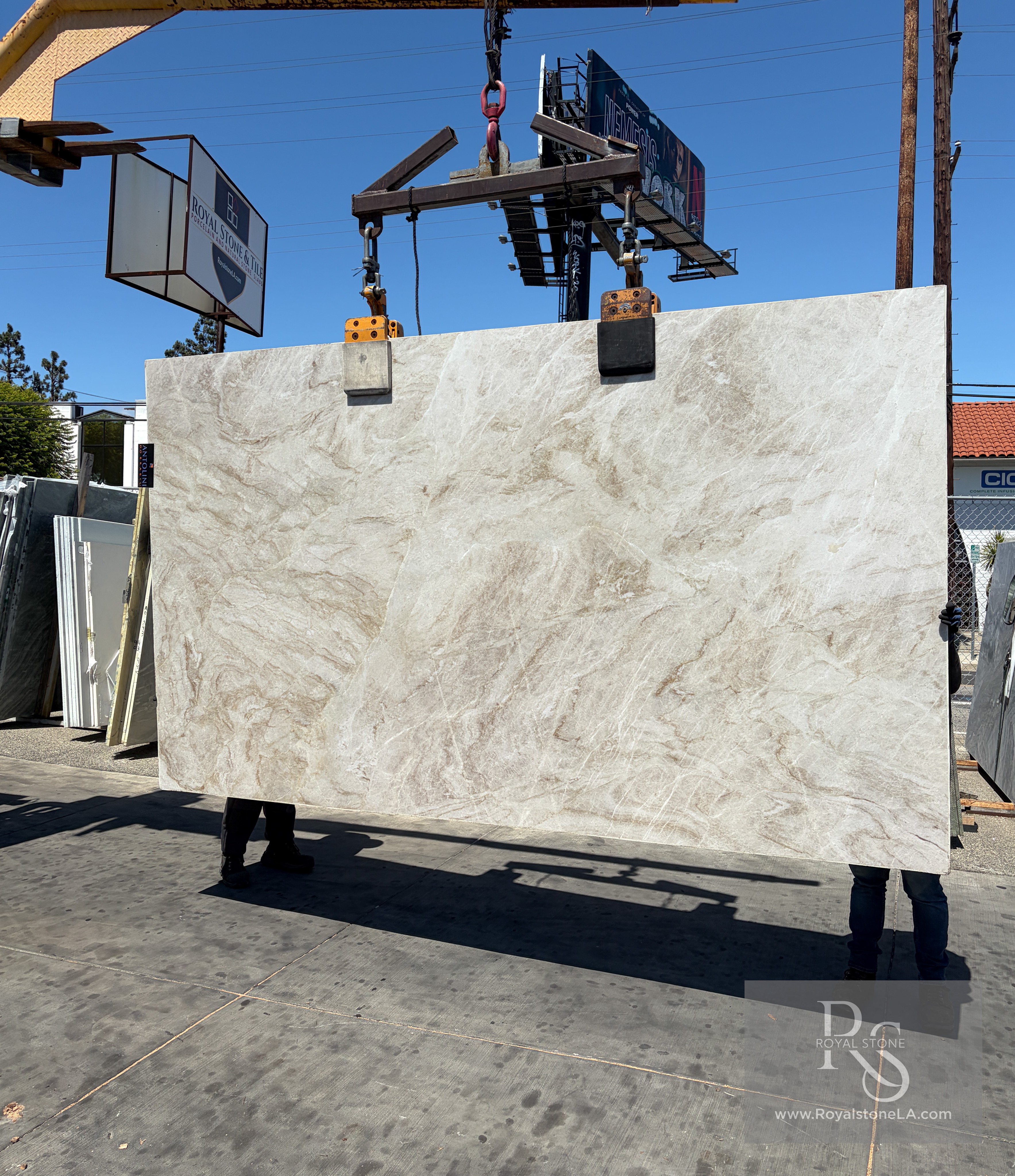 Antolini Taj Mahal Select AO758 polished quartzite slab lifted on the crane against blue sky, warm ivory field with soft taupe and caramel drift