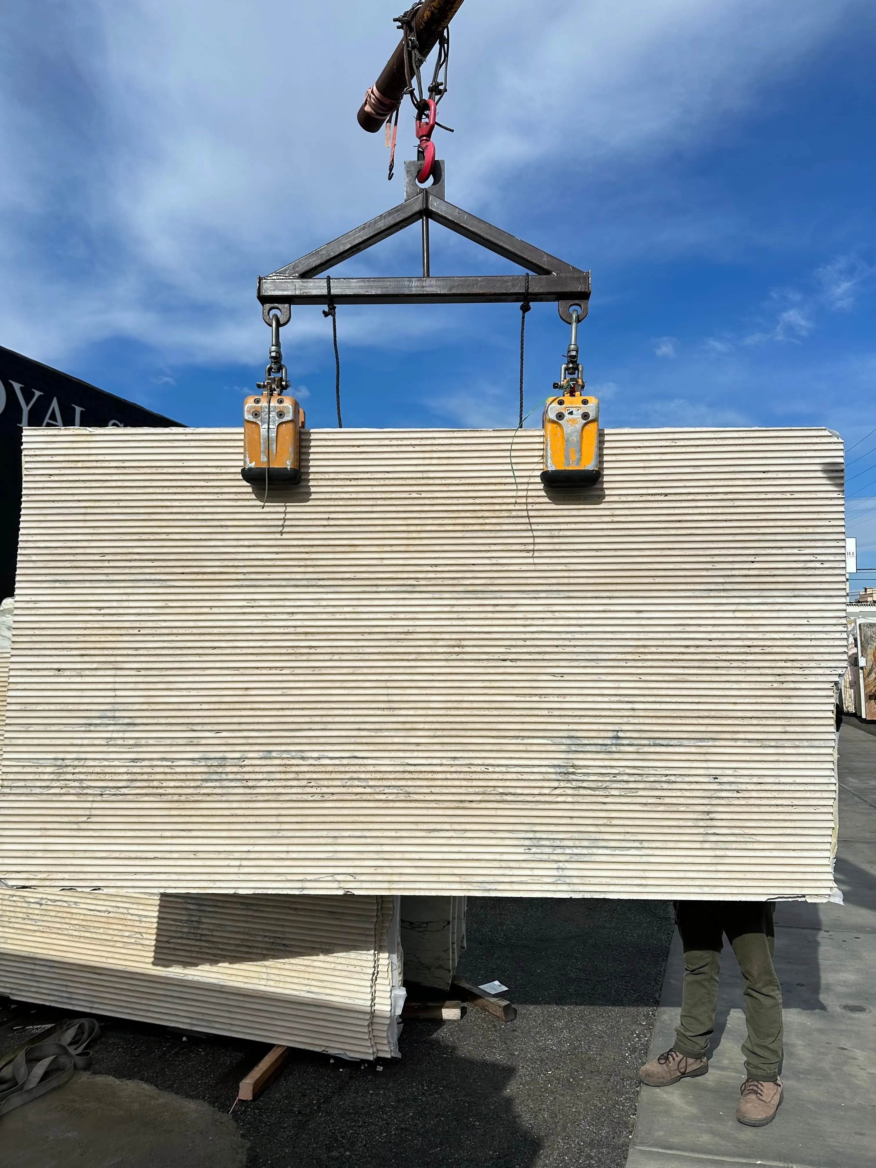 Antolini Travertine Premium slab with fluted finish on the crane at Royal Stone, ivory field with horizontal vein structure and close vertical ribbing