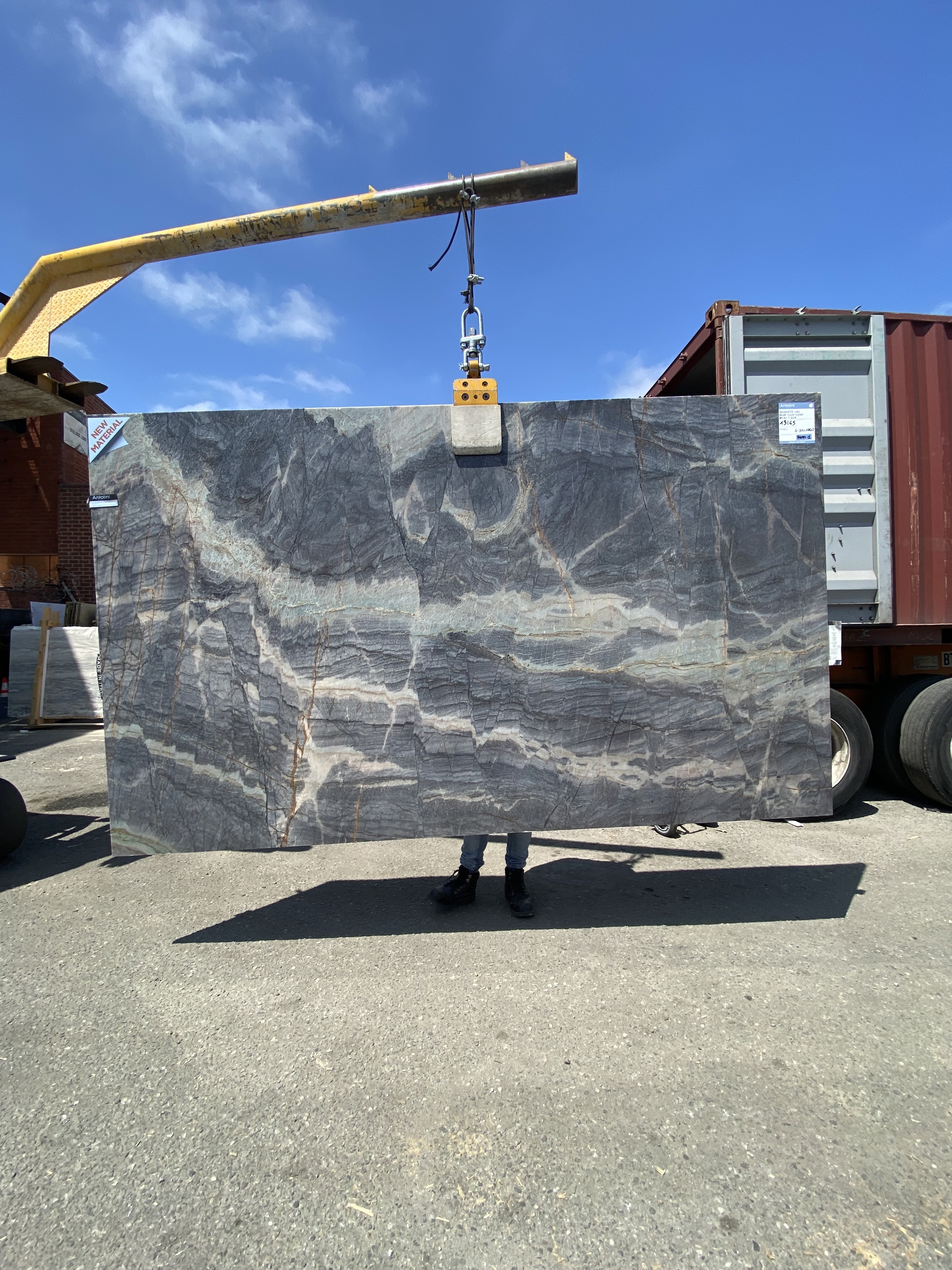 Antolini Blue Deep Liki quartzite slab on the crane at Royal Stone & Tile, deep storm grey-blue field with layered horizontal banding and faint gold trace veining, polished finish, 74 by 125 inches