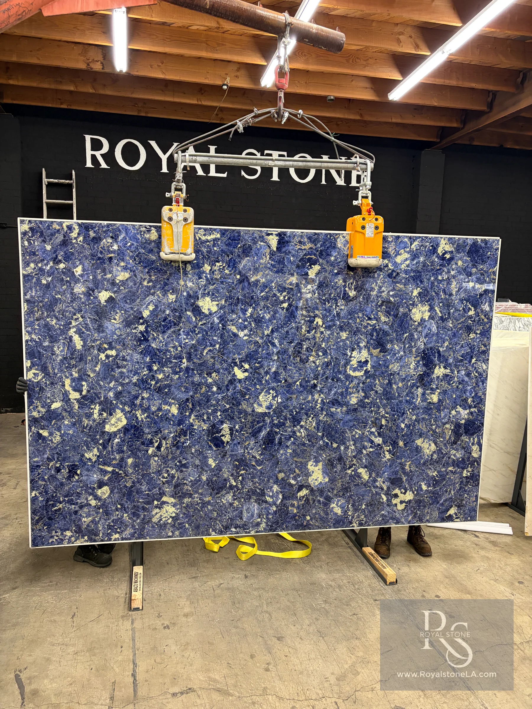 Blue Sodalite semi-precious slab reinforced with aluminum backing at 73 by 126 inches standing in the Royal Stone Los Angeles warehouse, deep royal-blue field with cream calcite patches and white veining