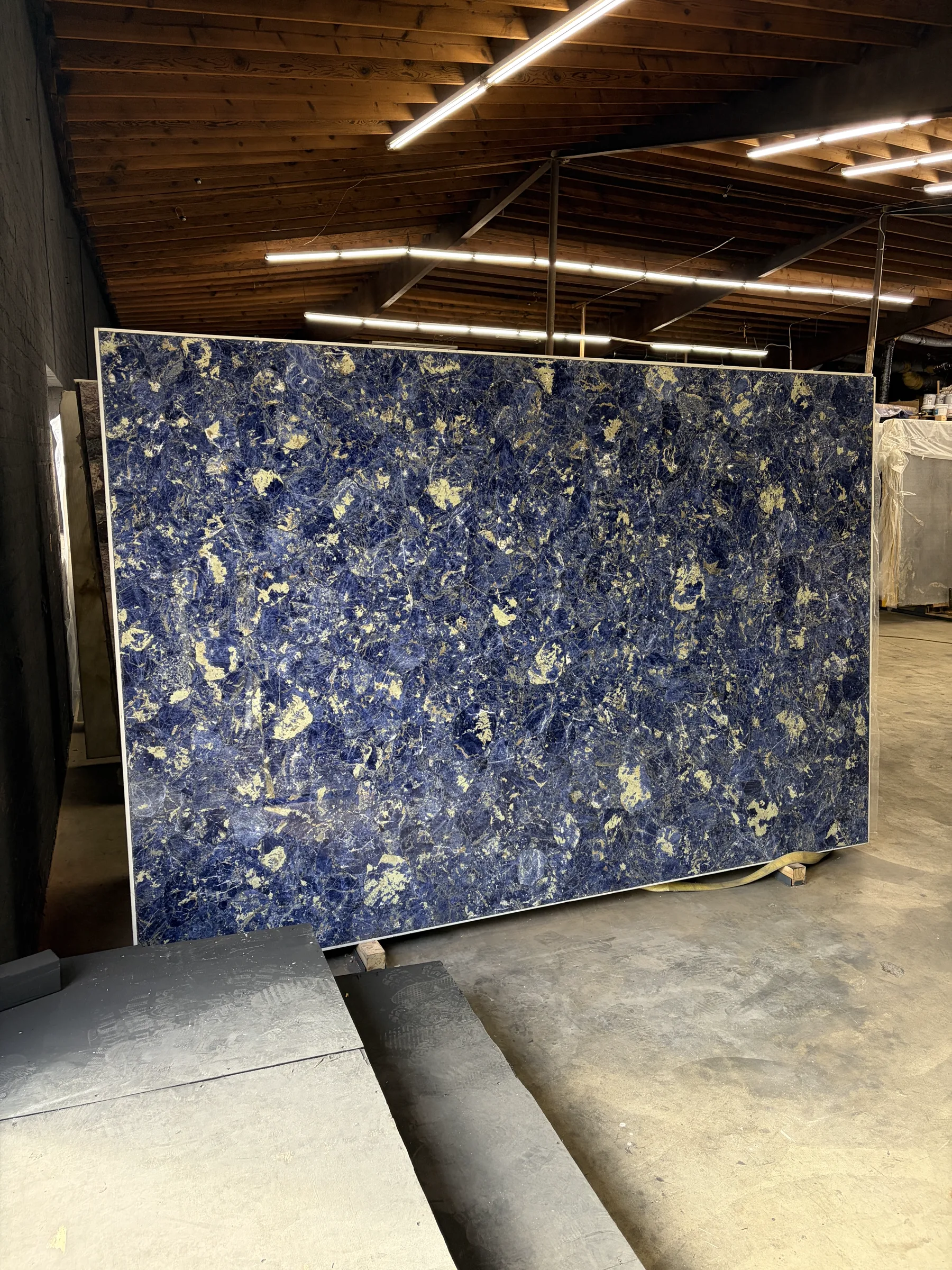 Blue Sodalite semi-precious slab reinforced with aluminum backing at 80 by 120 inches standing in the Royal Stone Los Angeles warehouse, deep royal-blue field with cream calcite patches and white veining