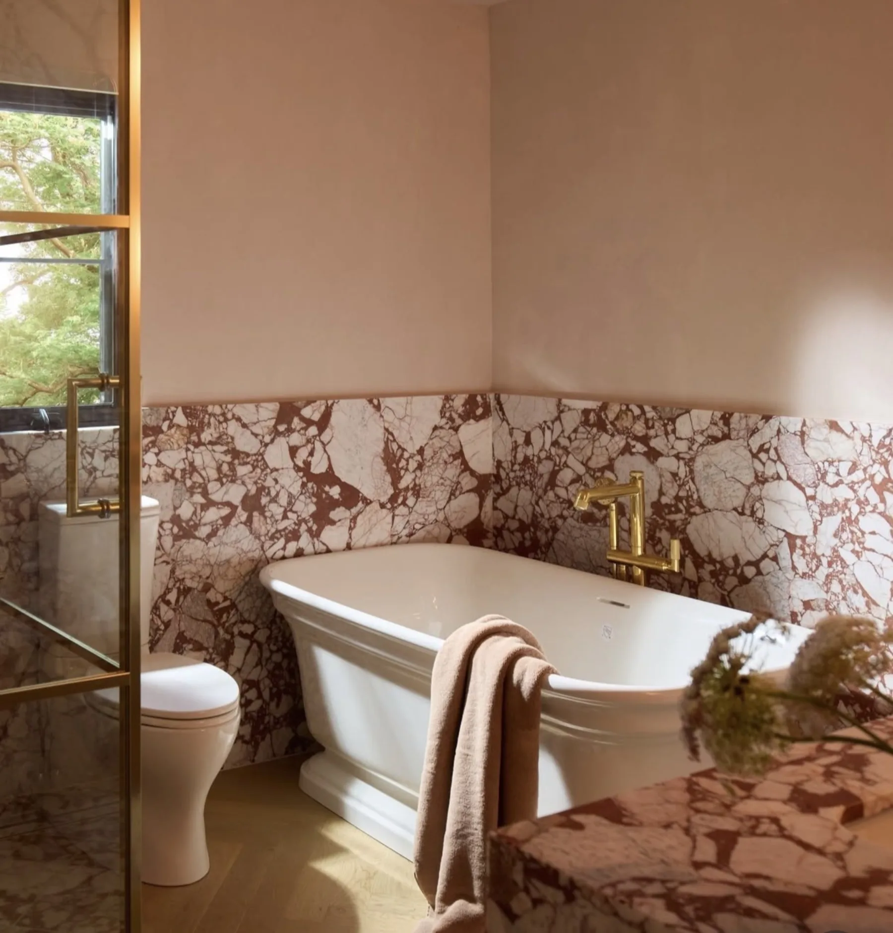 Freestanding white tub against a Calacatta Viola Rosso Extra marble wainscot wall with brass tub filler, plaster ceiling above the stone line