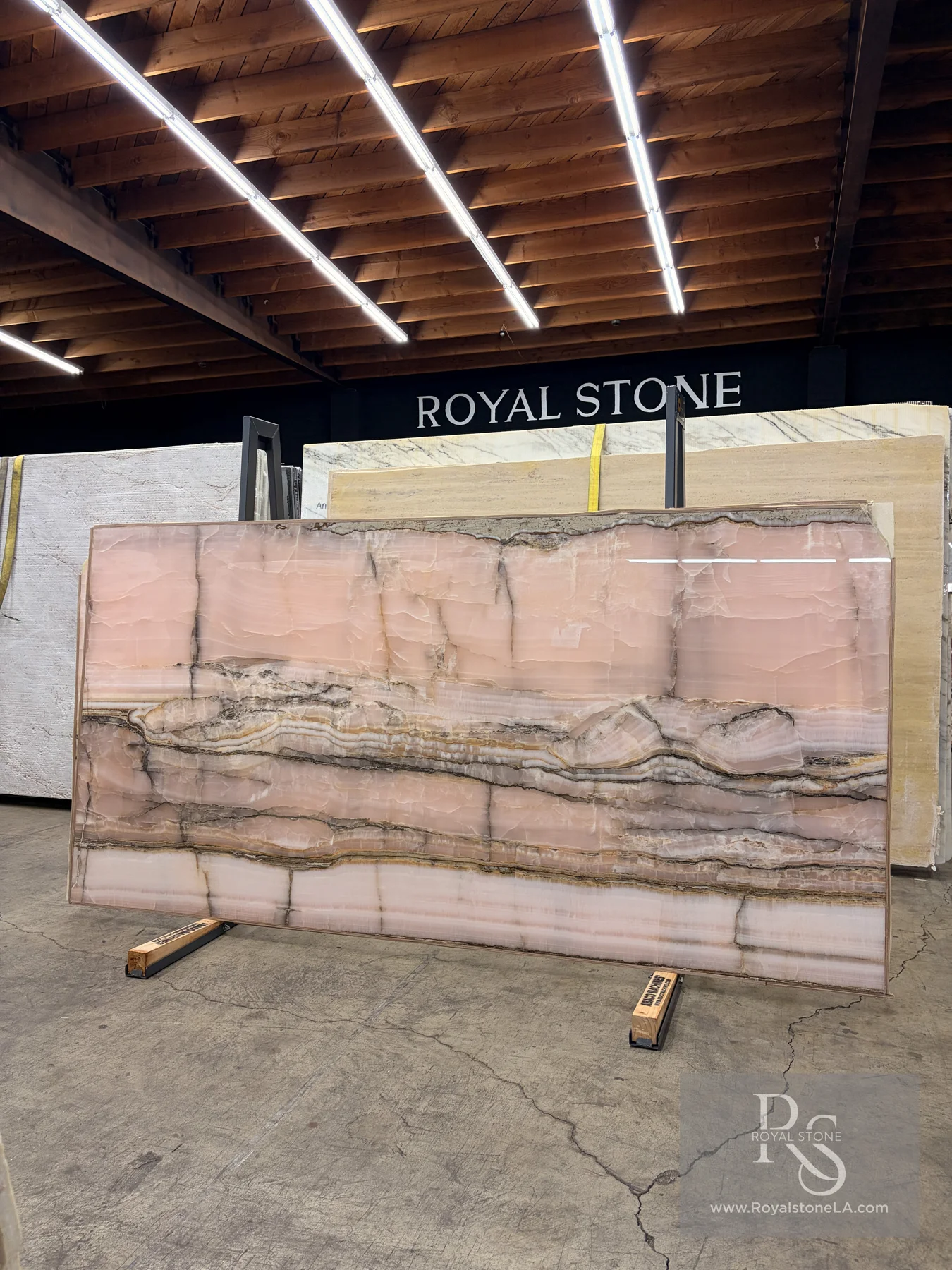 Chanel Pink Onyx Select polished slab, 55 by 110 inches, standing on the Royal Stone yard floor in Los Angeles, blush-pink body with cream, honey, and charcoal banding