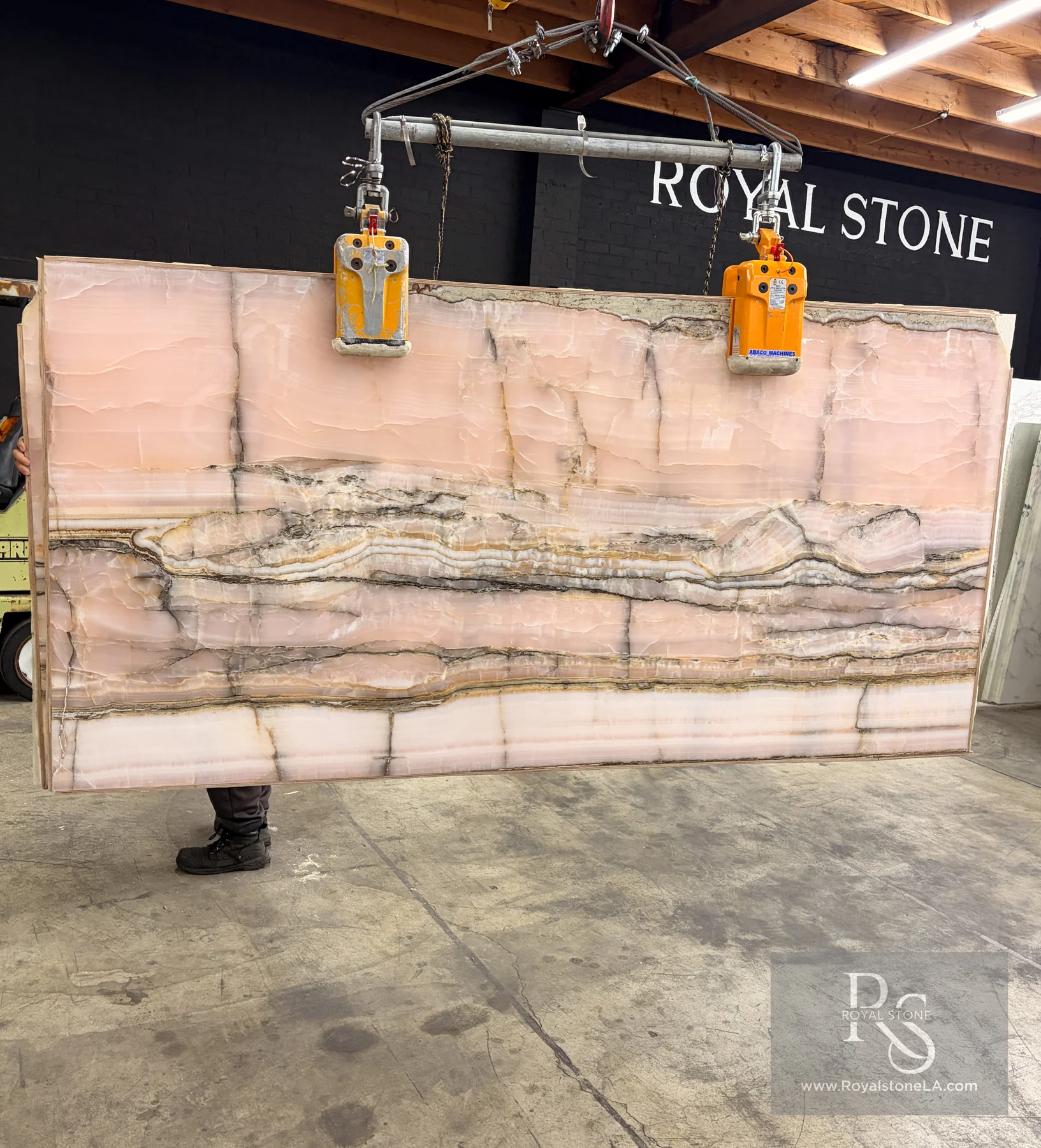 Chanel Pink Onyx Select polished slab, 55 by 110 inches, lifted on the crane at the Royal Stone yard in Los Angeles, blush-pink translucent body with cream, honey, and charcoal banding