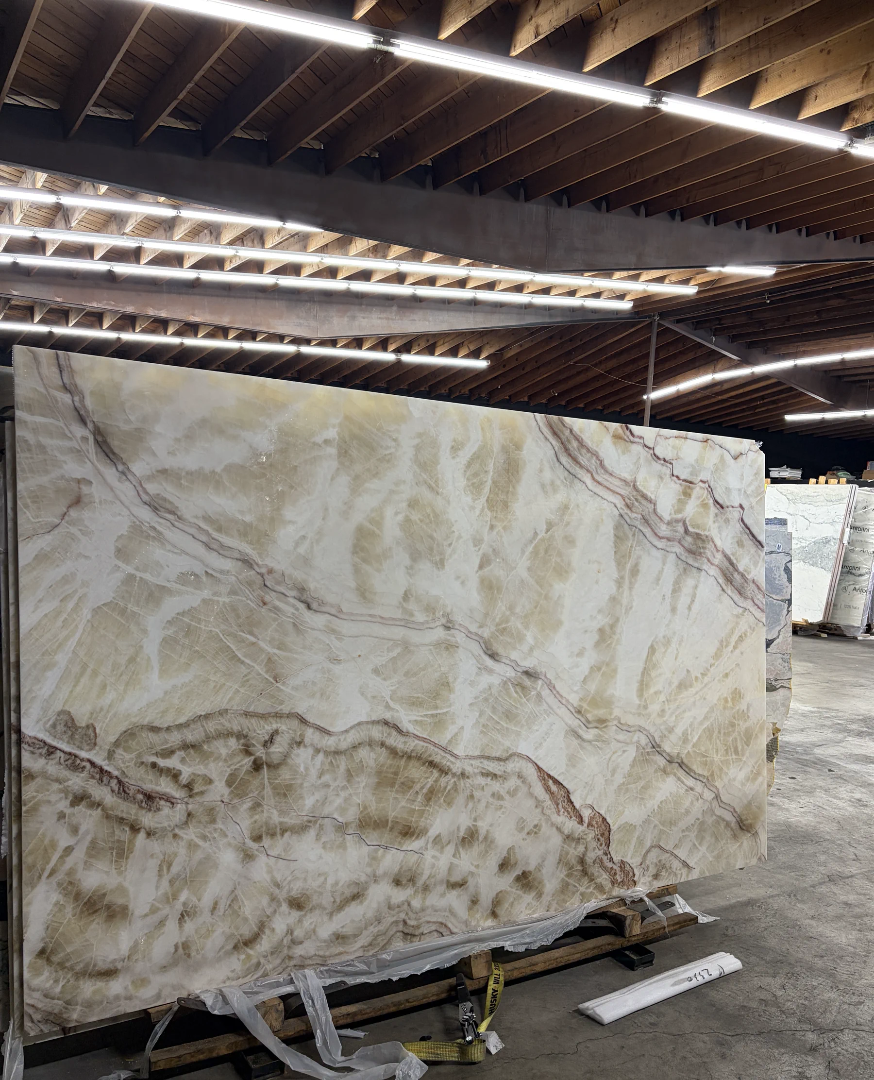 Channel White vein-cut onyx slab in the Royal Stone warehouse, showing its milky white-cream field and rust-red and amber veining