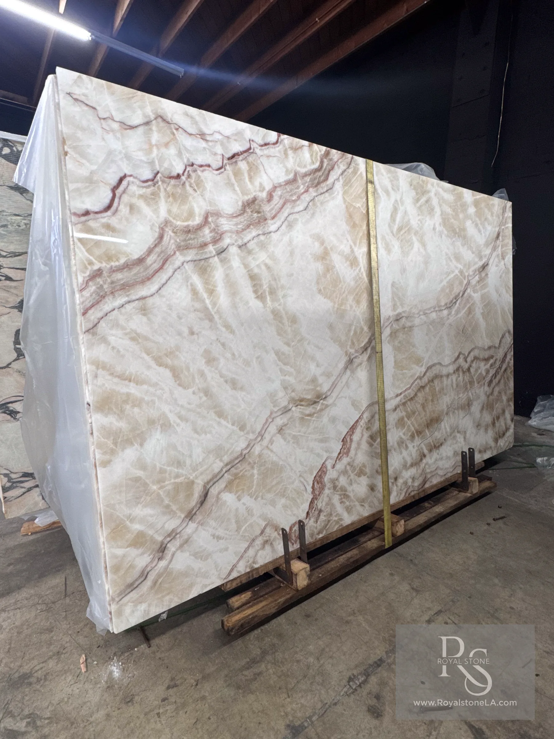 Channel White vein-cut onyx slab polished at 70 by 113 inches standing in the Royal Stone Los Angeles warehouse, milky white-cream translucent body with rust-red and amber veining