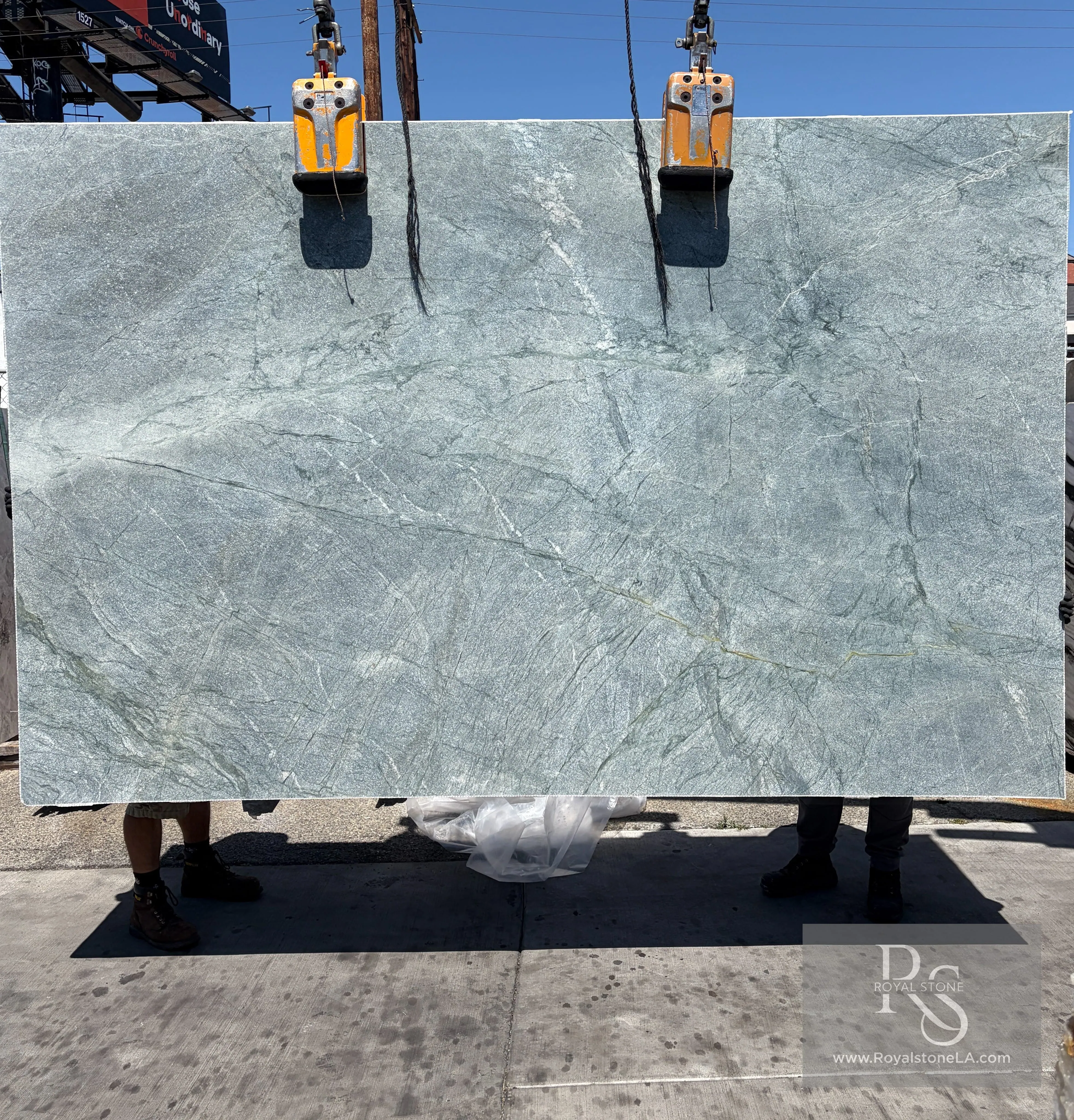 2cm Costa Smeralda quartzite slab in a heavy leather finish, 79 by 123 inches, with seafoam-green field and delicate white crystalline veining, lifted on the vacuum gantry at the Royal Stone Los Angeles yard