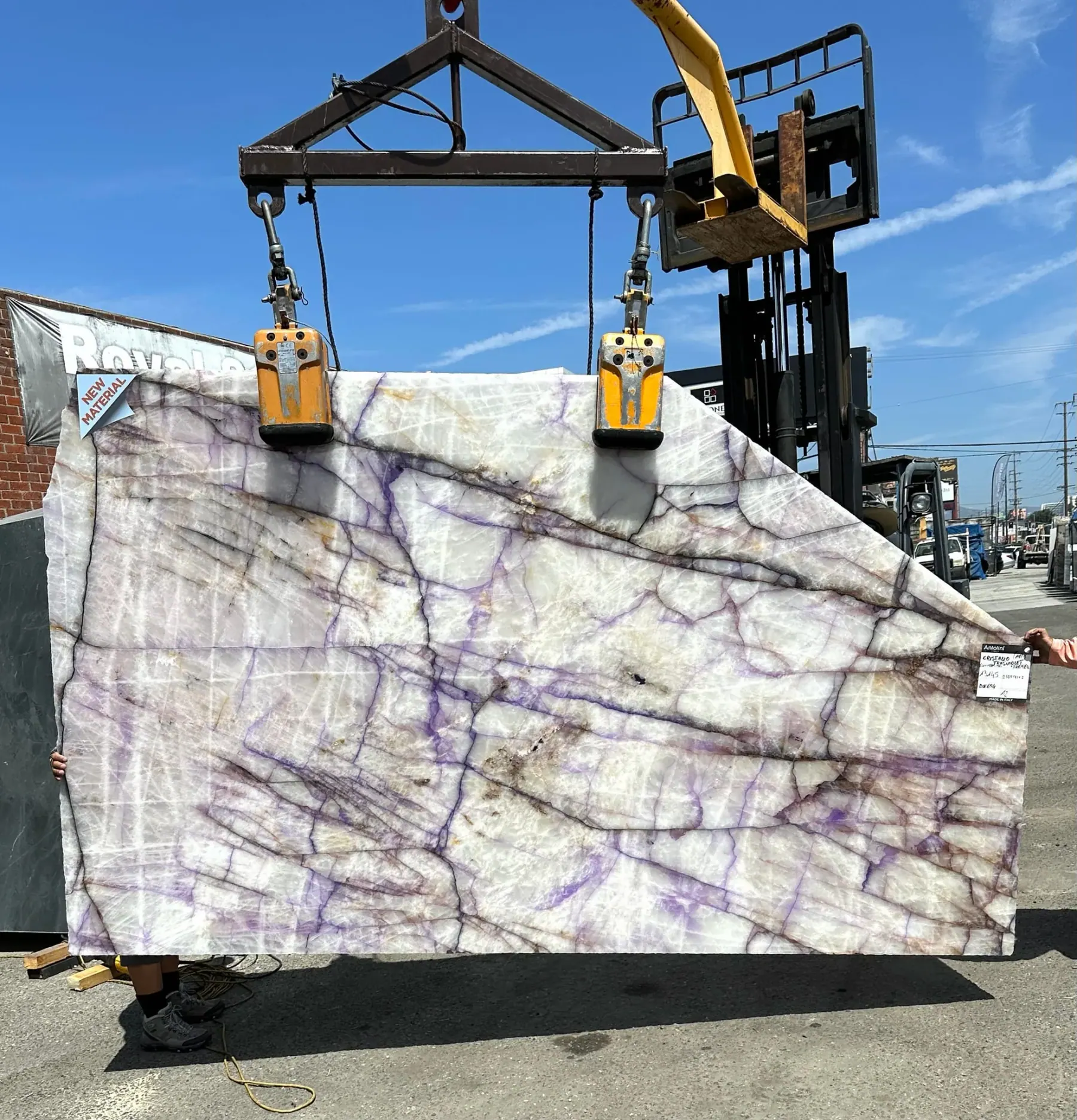 Antolini Cristallo Trasviolet polished translucent natural quartz slab lifted off the rack at Royal Stone in daylight, violet streaks and warm iron oxide threads on a clear white crystalline field