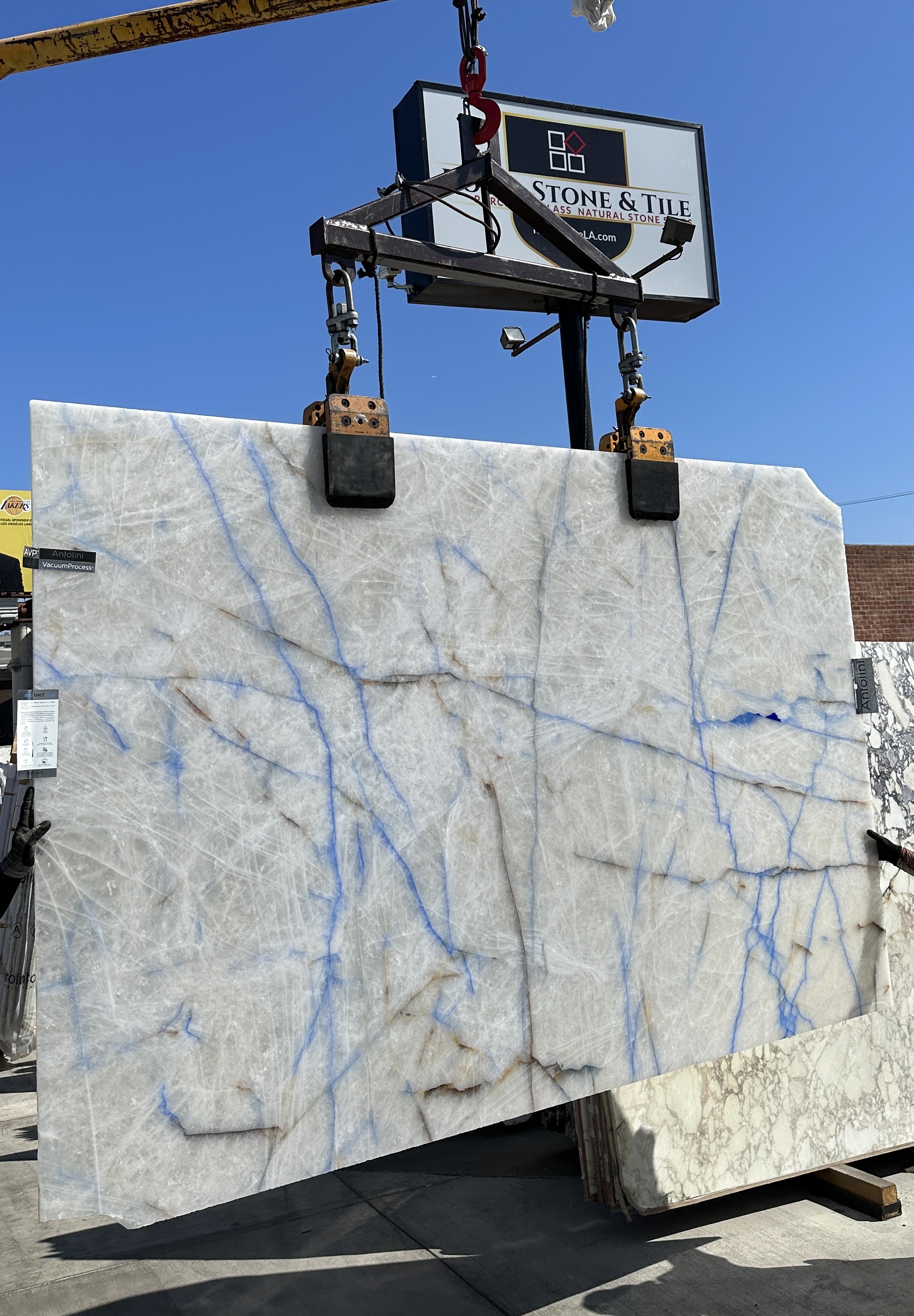 Antolini Cristallo Transazul quartzite slab on the crane, translucent white crystalline quartz field with delicate cobalt-blue veining, polished finish, AVP vacuum process treated, 75 by 116 inches