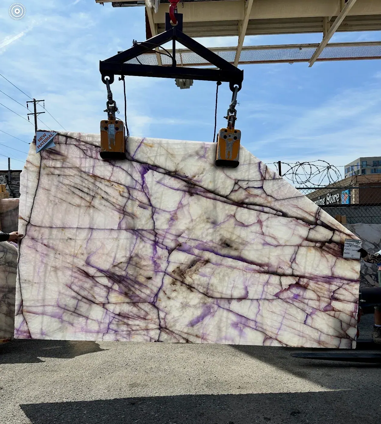 Antolini Cristallo Trasviolet slab held into the sun at the Royal Stone yard, violet veining glowing through a translucent white crystalline field