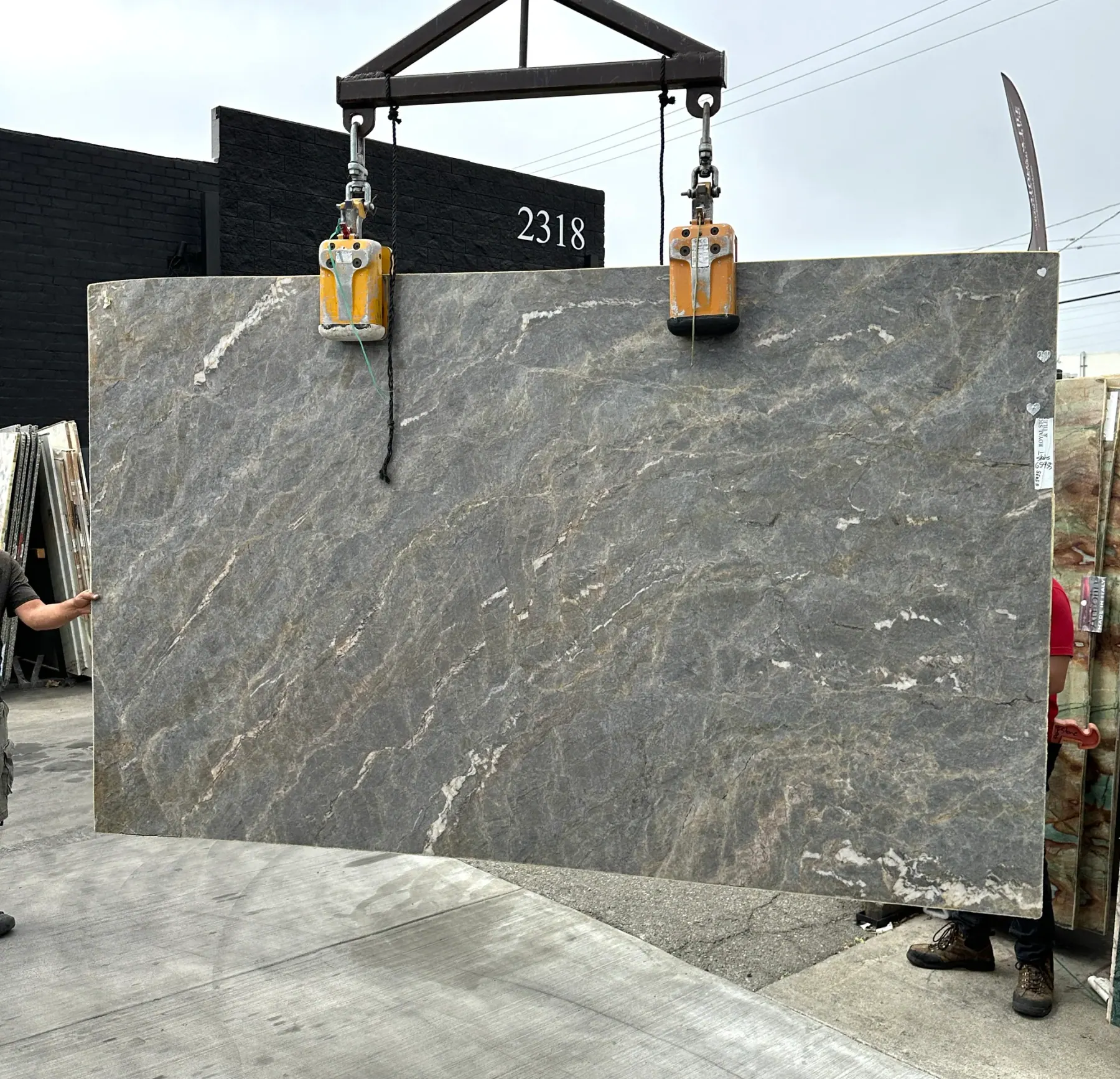 2cm Elysium Blue quartzite slab, 74 by 122 inches, polished finish with cool slate-blue body, warm caramel drift, and fine white quartz veining, lifted by crane outside Royal Stone at 2318 in Los Angeles