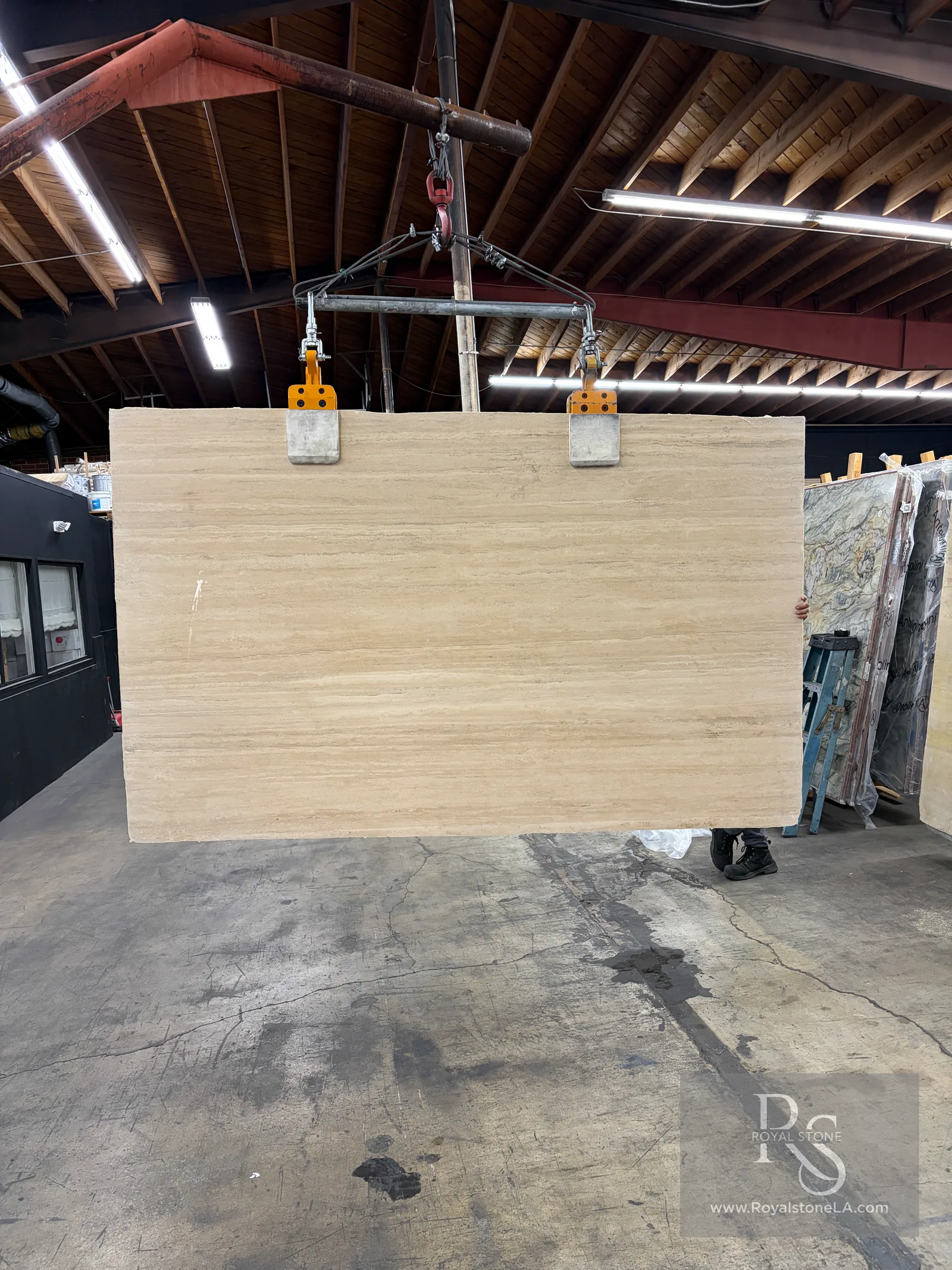 Second view of a super premium 2cm Italian Roman Travertine slab, vein cut, honed and filled, warm beige linear bands, hanging on the clamps at the Royal Stone yard in Los Angeles