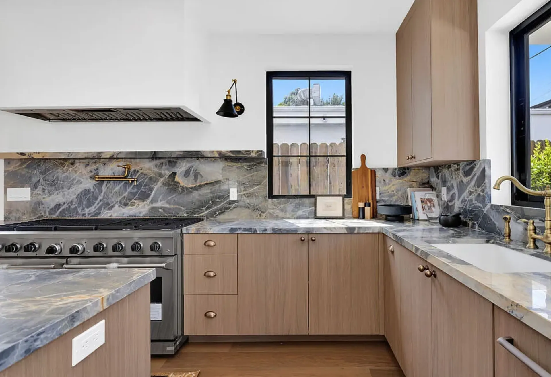 Portoro Gold Tempest polished marble kitchen backsplash, counters, and island with light oak cabinetry and brass fixtures