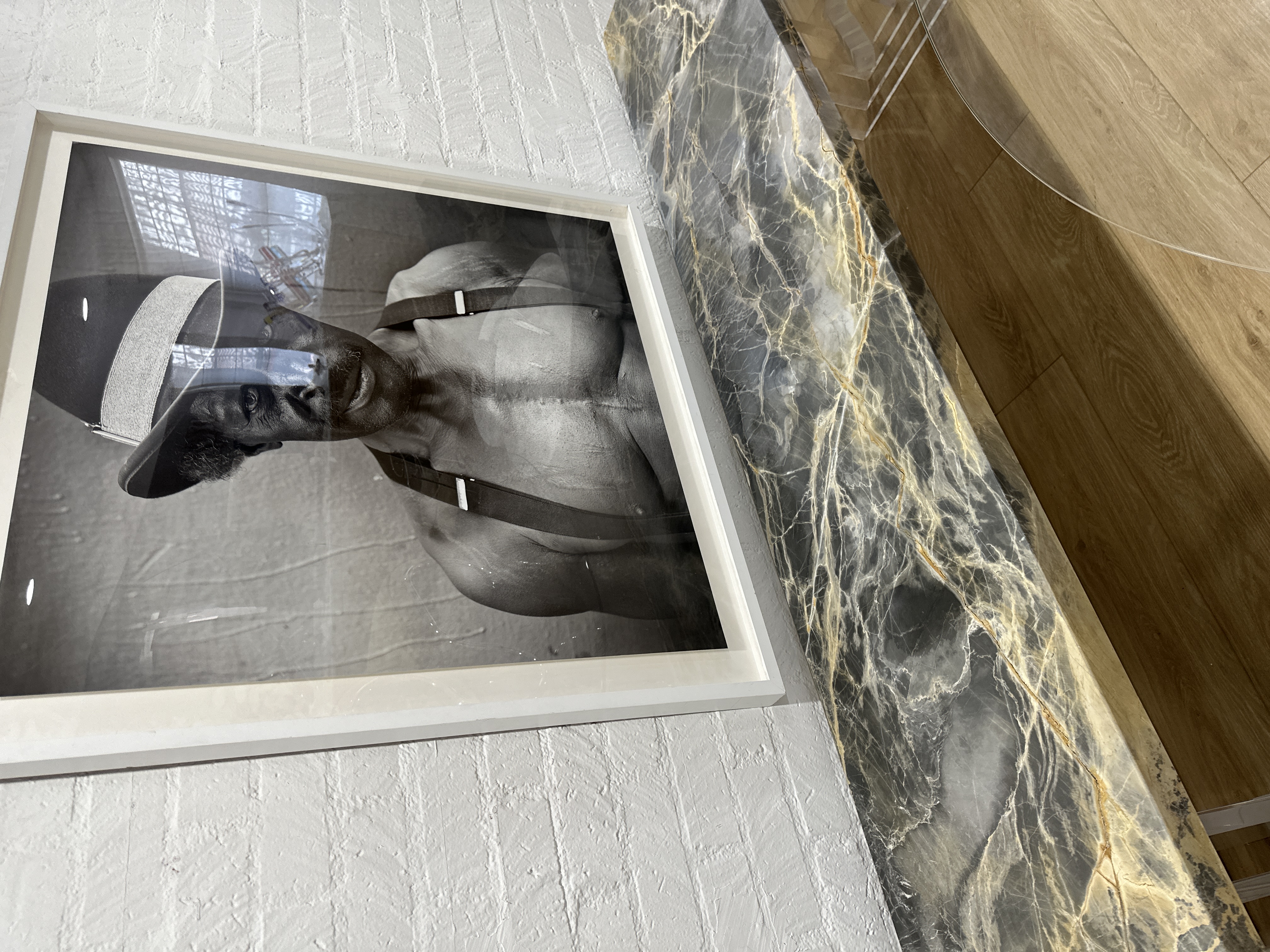 Portoro Gold Tempest marble installed as a long, low console-height ledge against a whitewashed brick wall, beneath a large black-and-white framed portrait — stormy gray field and gold drift read at full scale