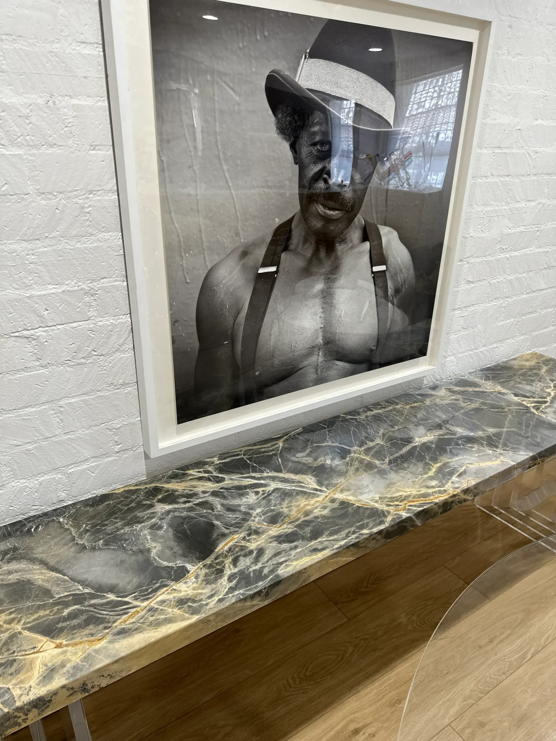 Portoro Gold Tempest marble installed as a long, low console-height ledge against a whitewashed brick wall, beneath a large black-and-white framed portrait — stormy gray field and gold drift read at full scale