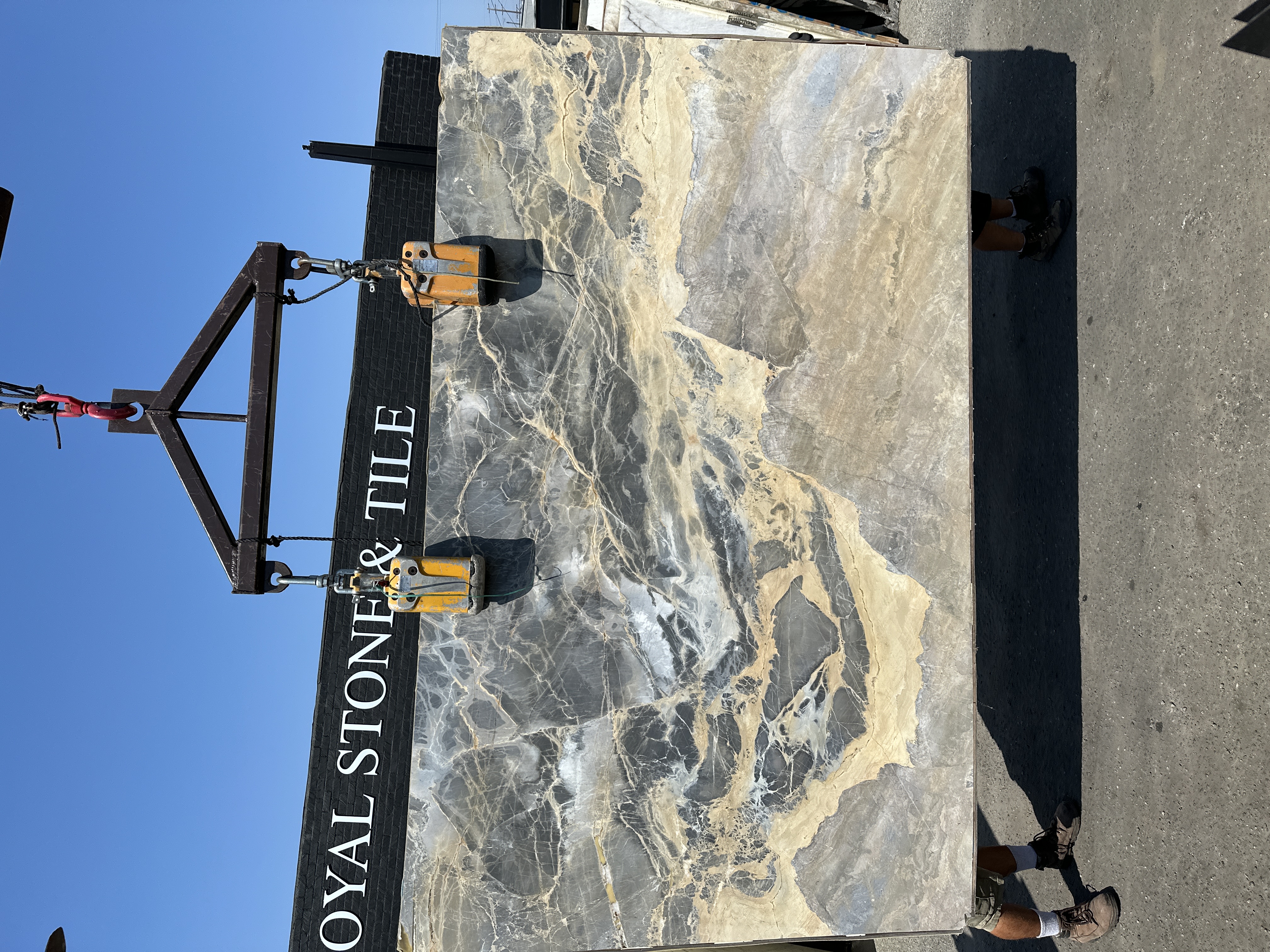 Portoro Gold Tempest marble slab, 78 by 126 inches, polished finish with stormy slate-gray field, molten gold and ochre drift, and fine white quartz veining, lifted by crane in front of the Royal Stone & Tile sign in Los Angeles