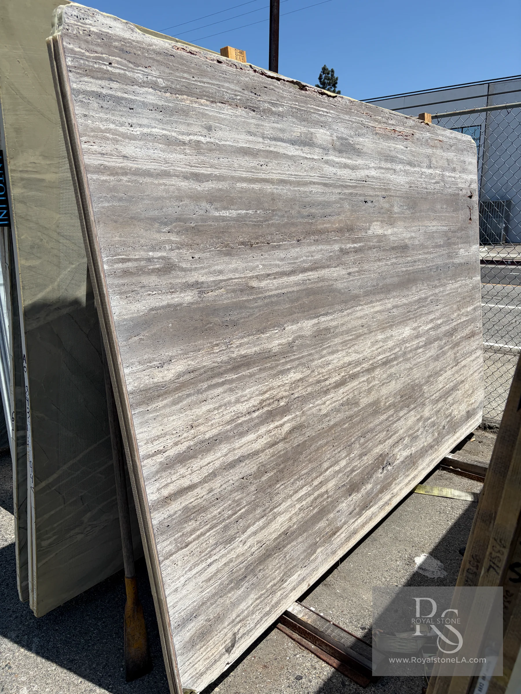 New 32-slab lot of 2cm Titanium Warm Shade Travertine, vein cut, filled and honed, shown in daylight at Royal Stone Los Angeles, 69 by 123 inches