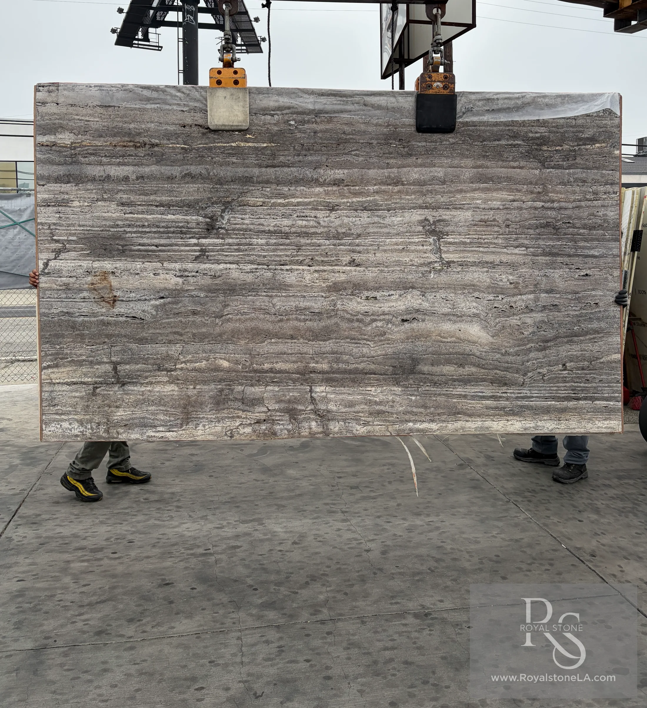 2cm Travertino Titanium Charcoal vein cut, honed and unfilled natural stone slab at Royal Stone Los Angeles, cool silver-grey and pewter horizontal stratification with iron-rust passages, lifted on overhead crane, 73 by 122 inches
