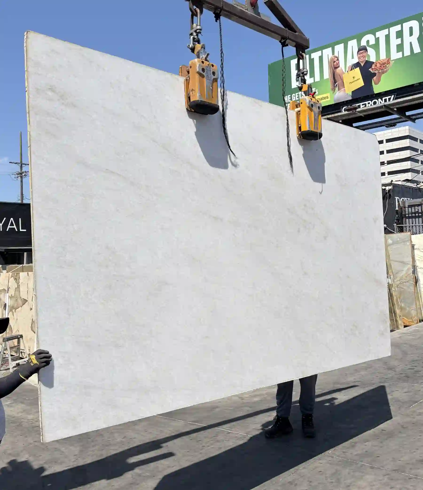 2cm Crystal White Supreme honed quartzite slab lifted by crane clamps in the Royal Stone yard, quiet white field in full daylight, Los Angeles