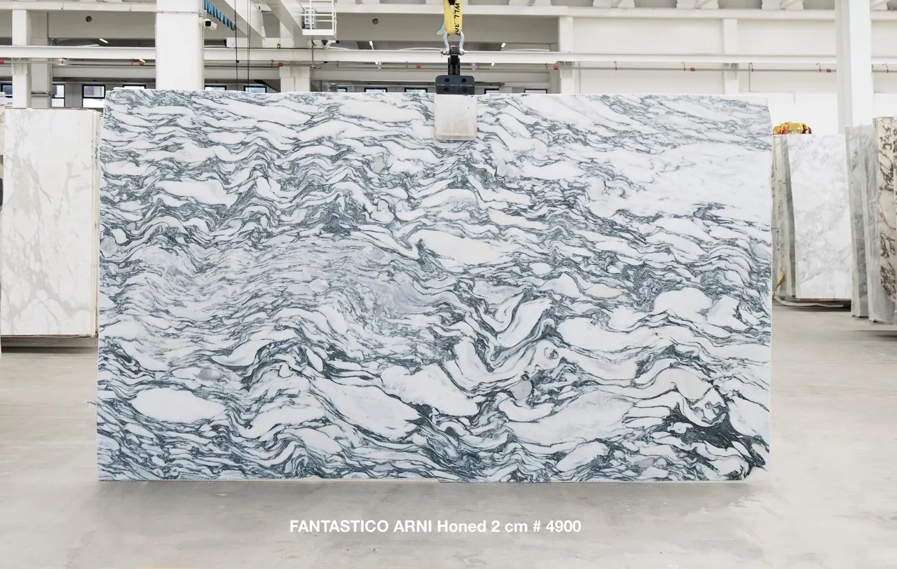 Fantastico Arni Honed 2cm marble slab, 130" × 76", lifted on overhead crane at the factory — white field crossed by sweeping blue, charcoal, and pale grey horizontal veining