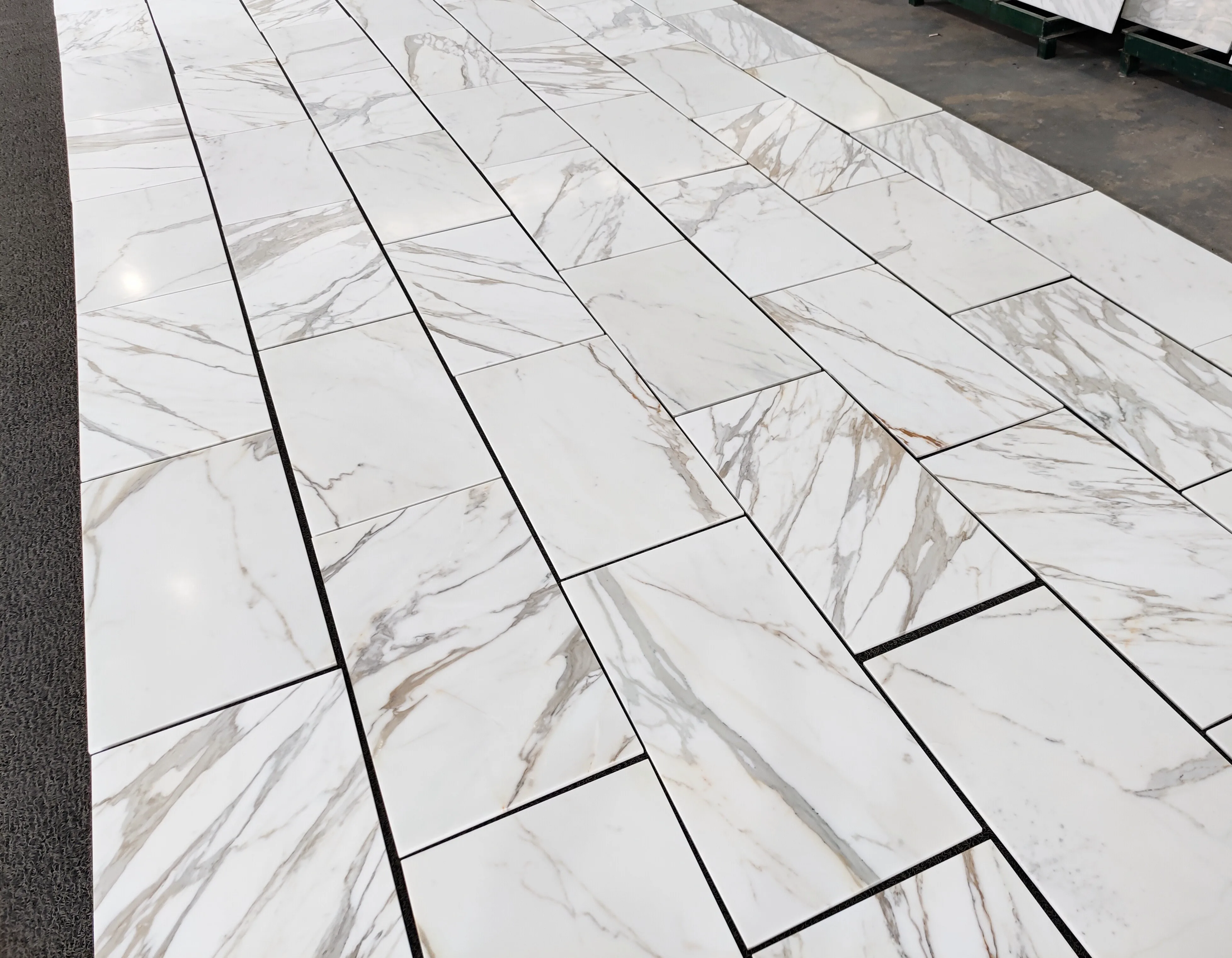 Italian Calacatta Gold marble 12 by 24-inch tile laid out in long rows on the Royal Stone yard floor, showing the warm gold veining running through the brighter May marble