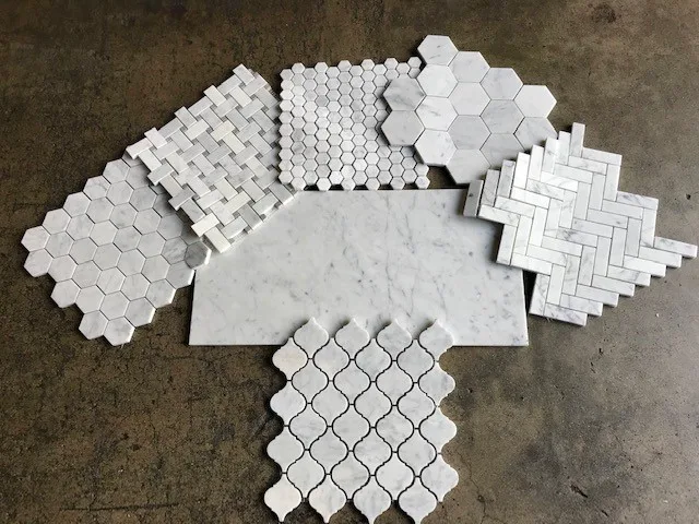 Honed Italian Carrara White marble field tile with a mixed-format mosaic sample set above it, photographed on concrete