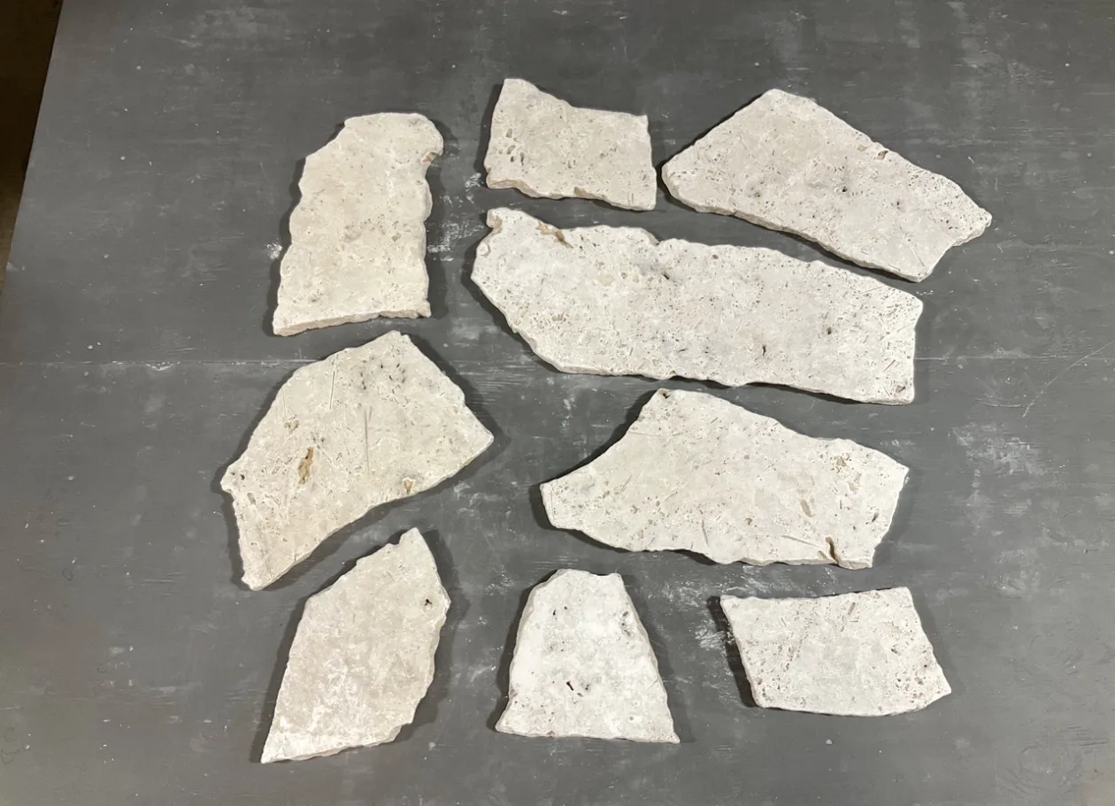 Ivory Unfilled 2cm Roman travertine flagstone pieces laid out on a concrete floor, showing the irregular broken shapes and cream-ivory unfilled face