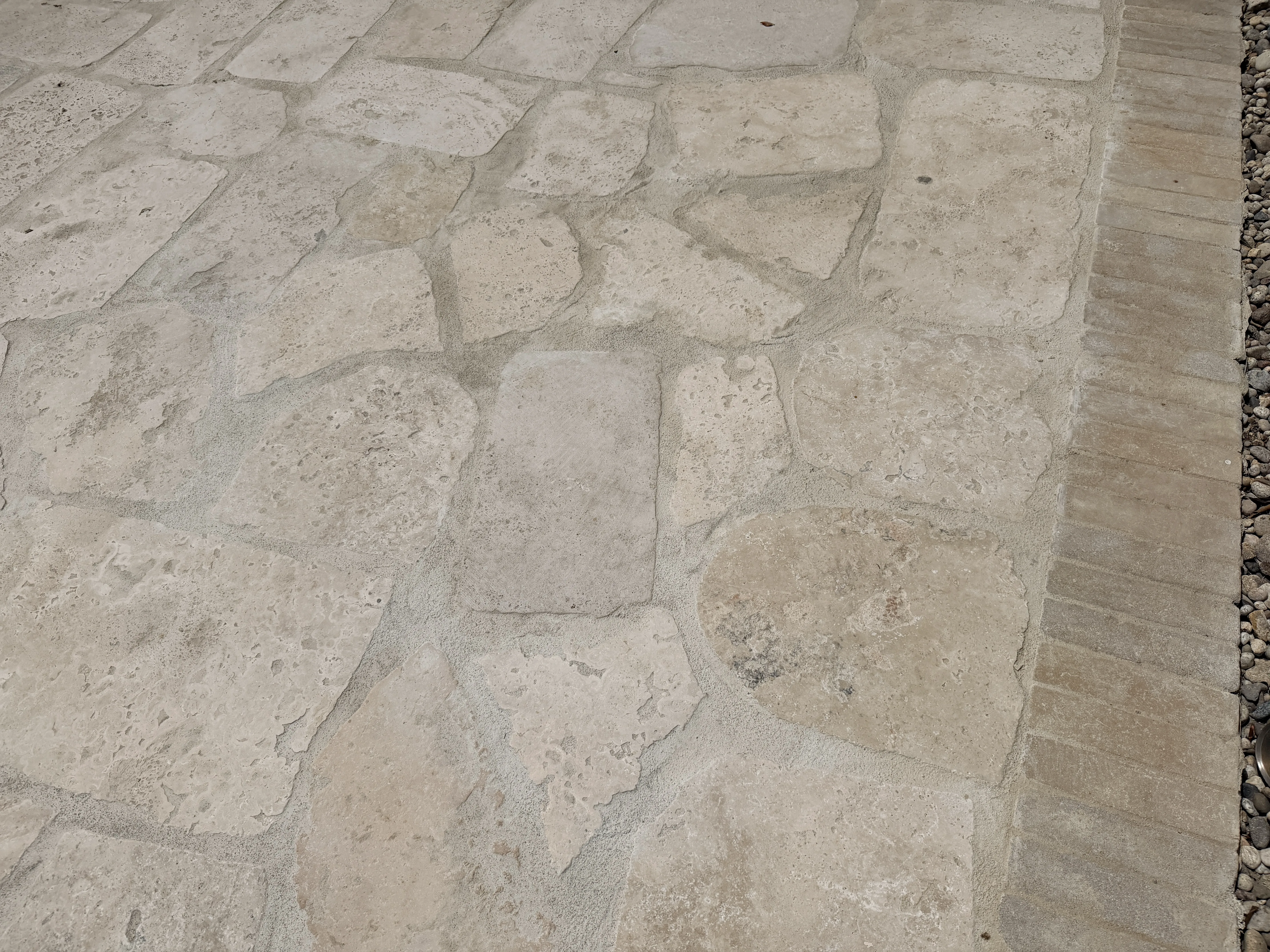 Random broken 2cm unfilled Roman travertine flagstone installed as a Los Angeles patio floor in irregular fitted shapes, with a wooden bench set into the stone field and a lavender border