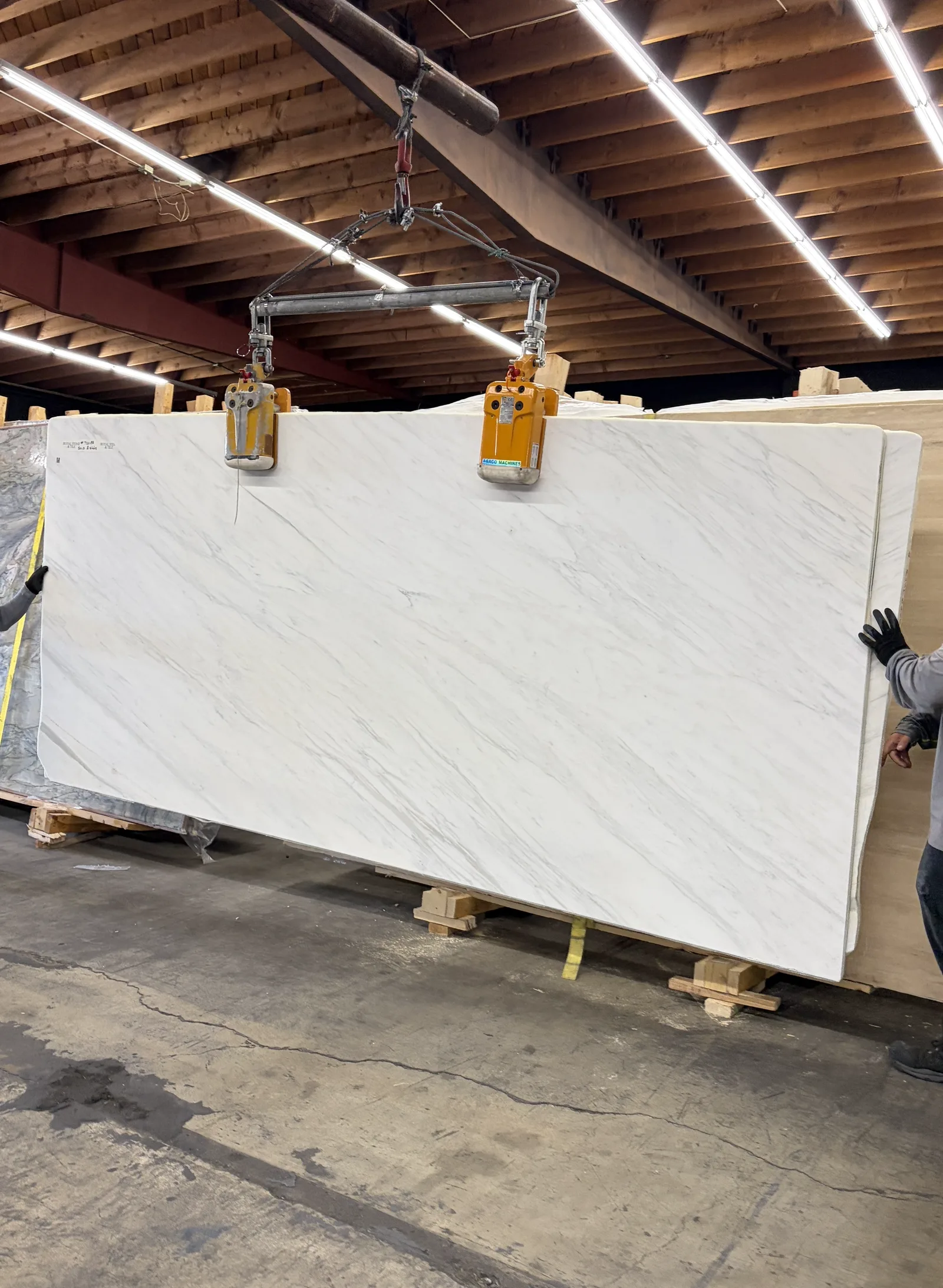 A 2cm Calacatta Caldia Soft White marble slab from lot PLST1418 being lifted by crane clamps at the Royal Stone yard in Los Angeles, soft white field with feathery gray veining