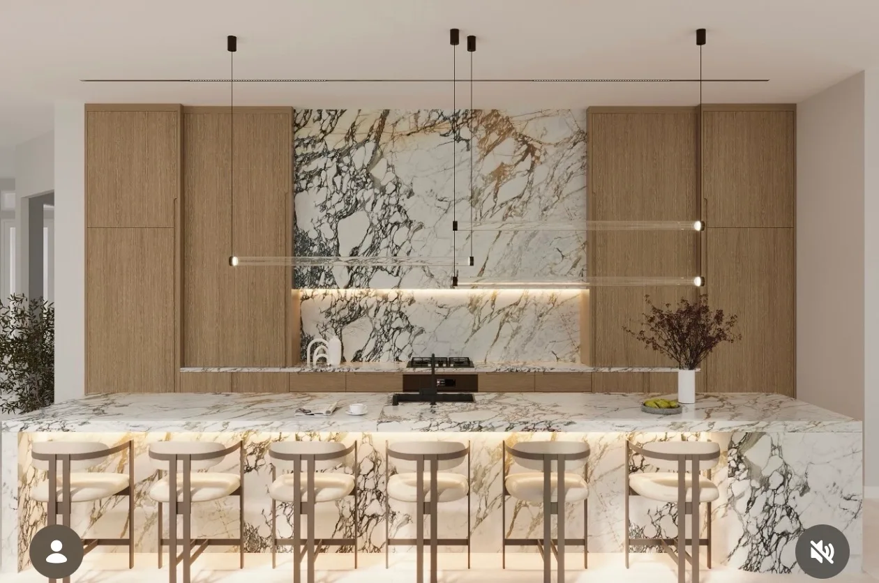 Long Calacatta marble bar-height island with bookmatched backsplash feature wall and oak millwork surround.