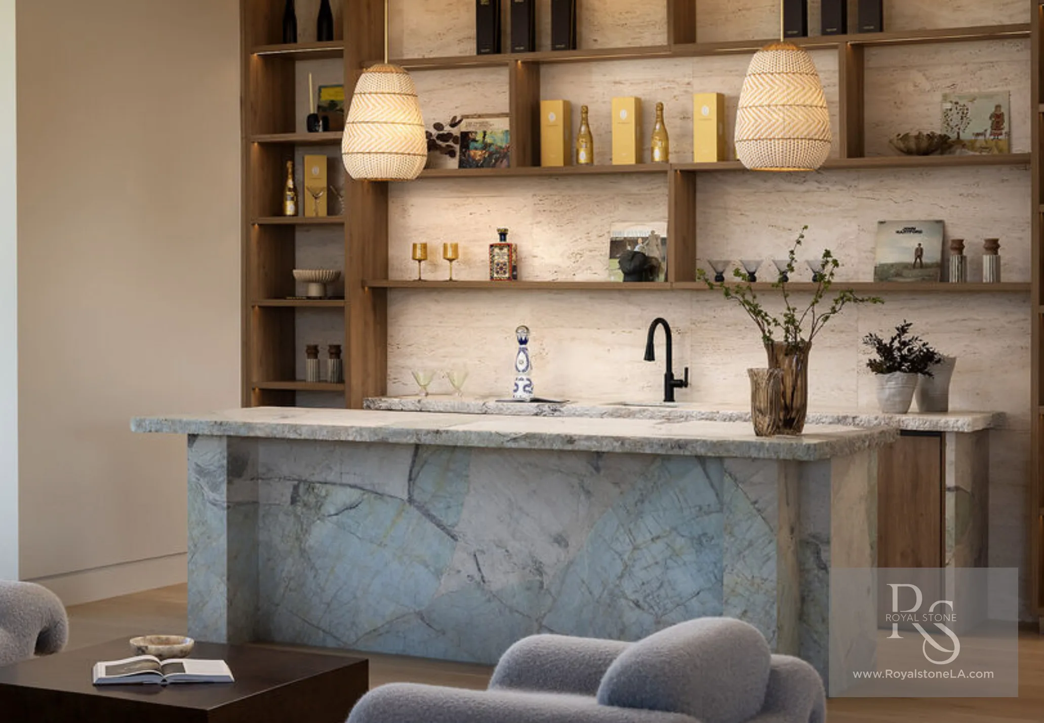Lounge bar at 1360 Laurel Way in Beverly Hills — a monolithic island clad in Antolini Patagonia Tiffany quartzite with a riven rock finish, its pale aqua-green crystalline field threaded with grey and gold veins, paired with a travertine backsplash, open oak shelving with champagne and art books, and woven pendant lights.