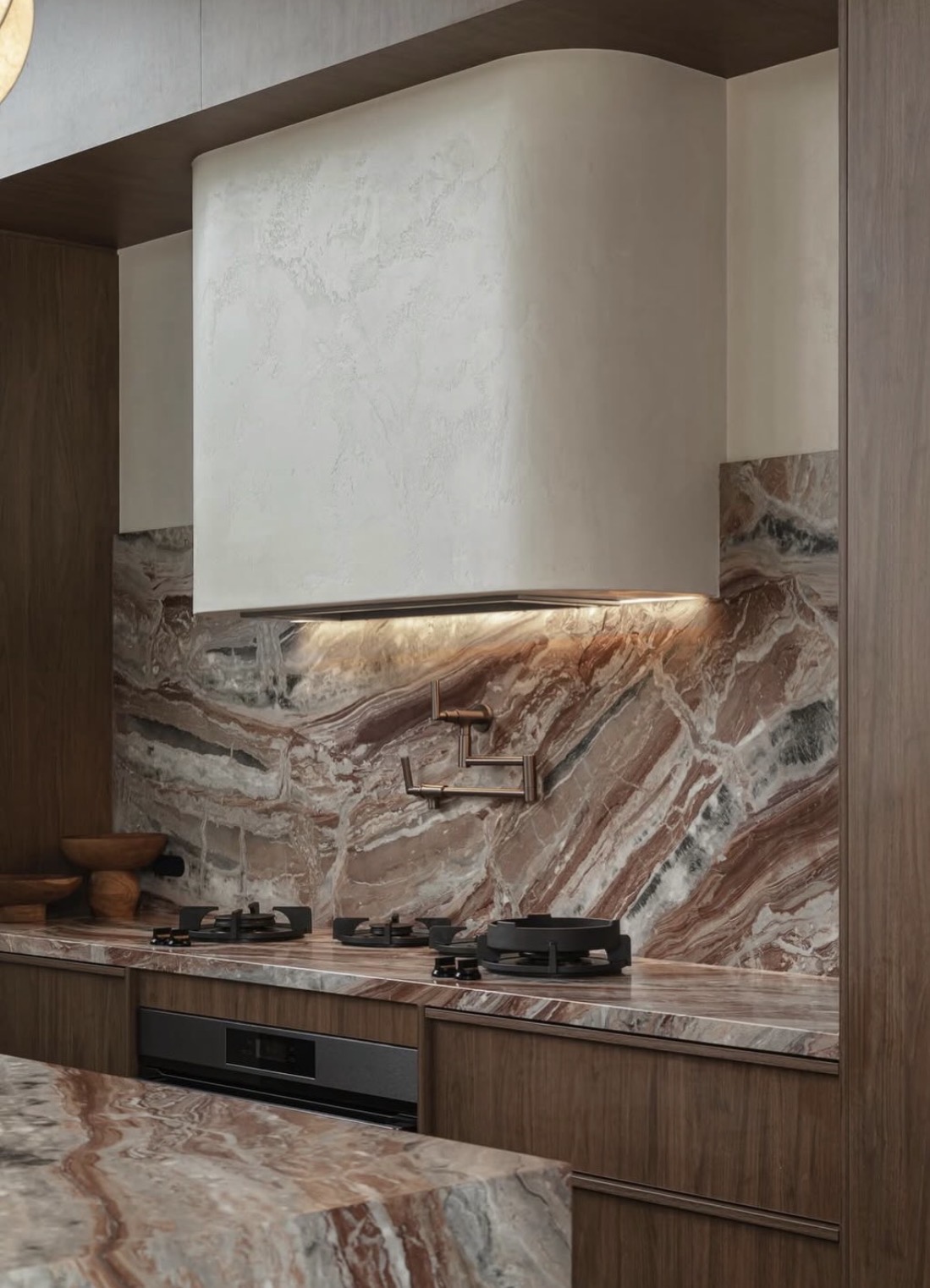 Kitchen range wall clad in Viola Arabescato Orobico Rosso marble — full-height slab backsplash threaded with rust, plum, and forest-green veining flowing diagonally across the wall, a plaster hood with integrated under-light, antique brass pot-filler, and matching Viola Orobico Rosso counter and island in walnut millwork.