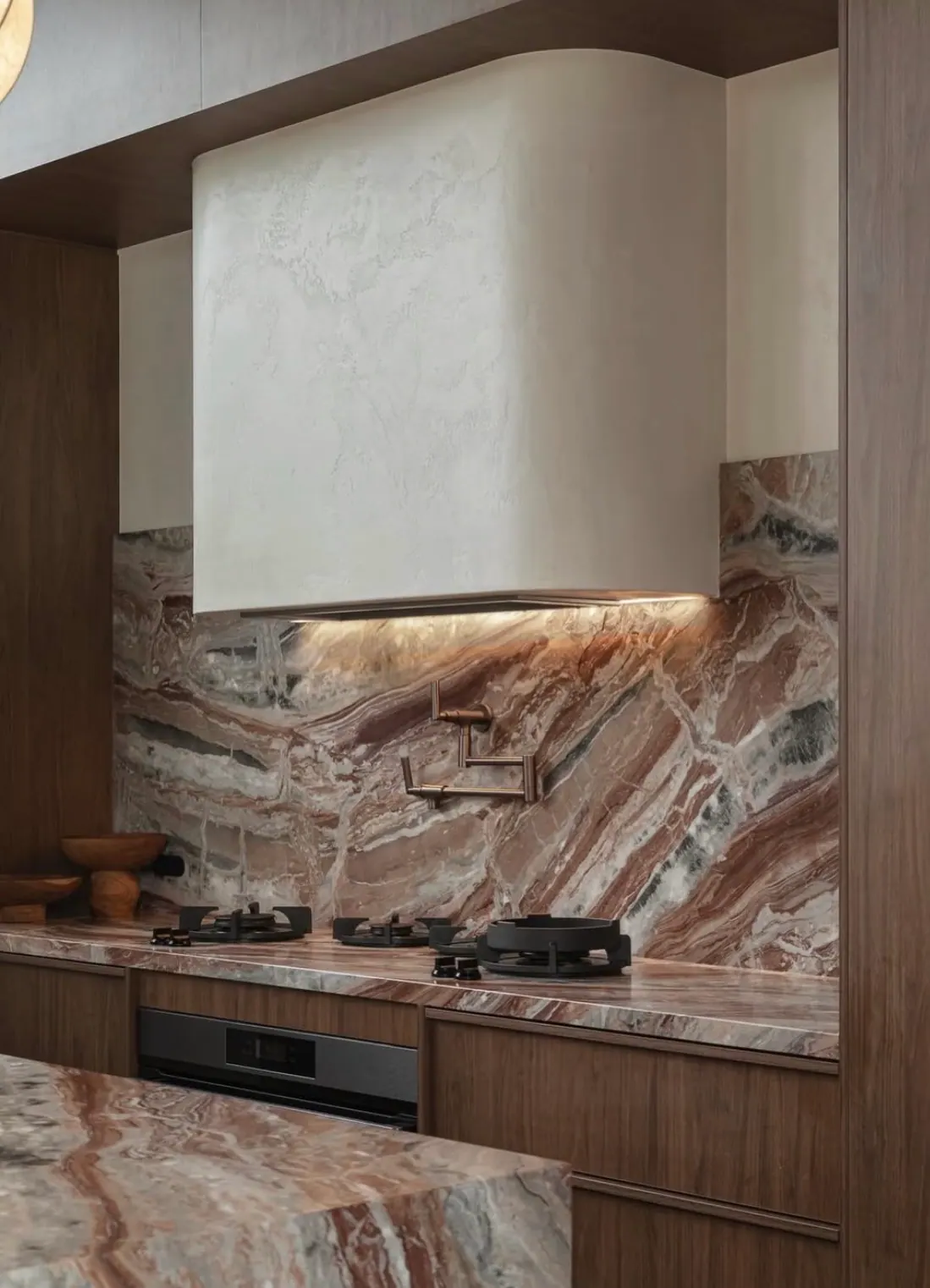 Kitchen range wall clad in Viola Arabescato Orobico Rosso marble — full-height slab backsplash threaded with rust, plum, and forest-green veining flowing diagonally across the wall, a plaster hood with integrated under-light, antique brass pot-filler, and matching Viola Orobico Rosso counter and island in walnut millwork.