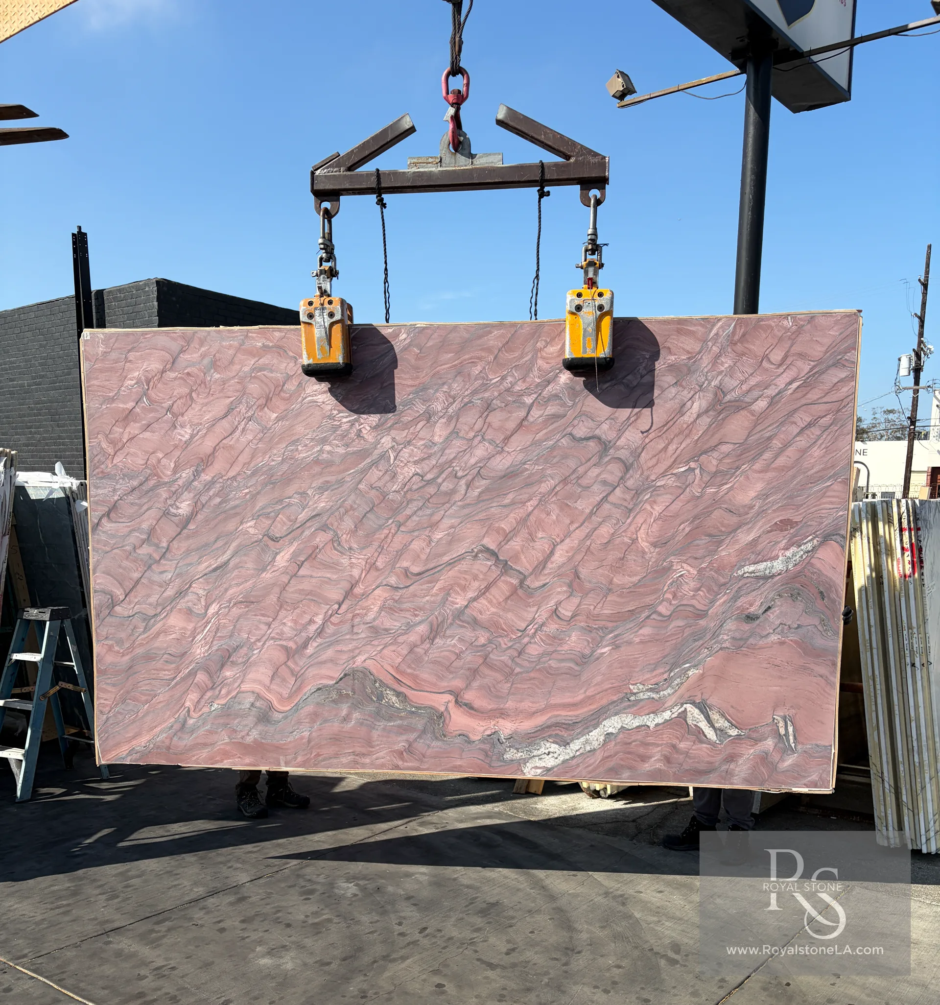 2cm Fusion Red Revolution honed quartzite slab, 78 by 130 inches, deep rose and mauve brecciated field with a striking white quartz seam at the lower edge, lifted on overhead crane at the Royal Stone yard in Los Angeles