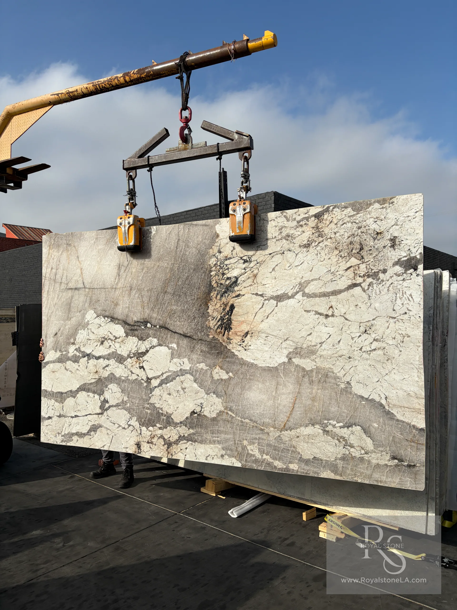 2cm Patagonia Alabastro honed quartzite slab, 80 by 138 inches, soft pink-grey translucent field with dramatic white cloud formations and warm veining, lifted on overhead crane at the Royal Stone yard in Los Angeles