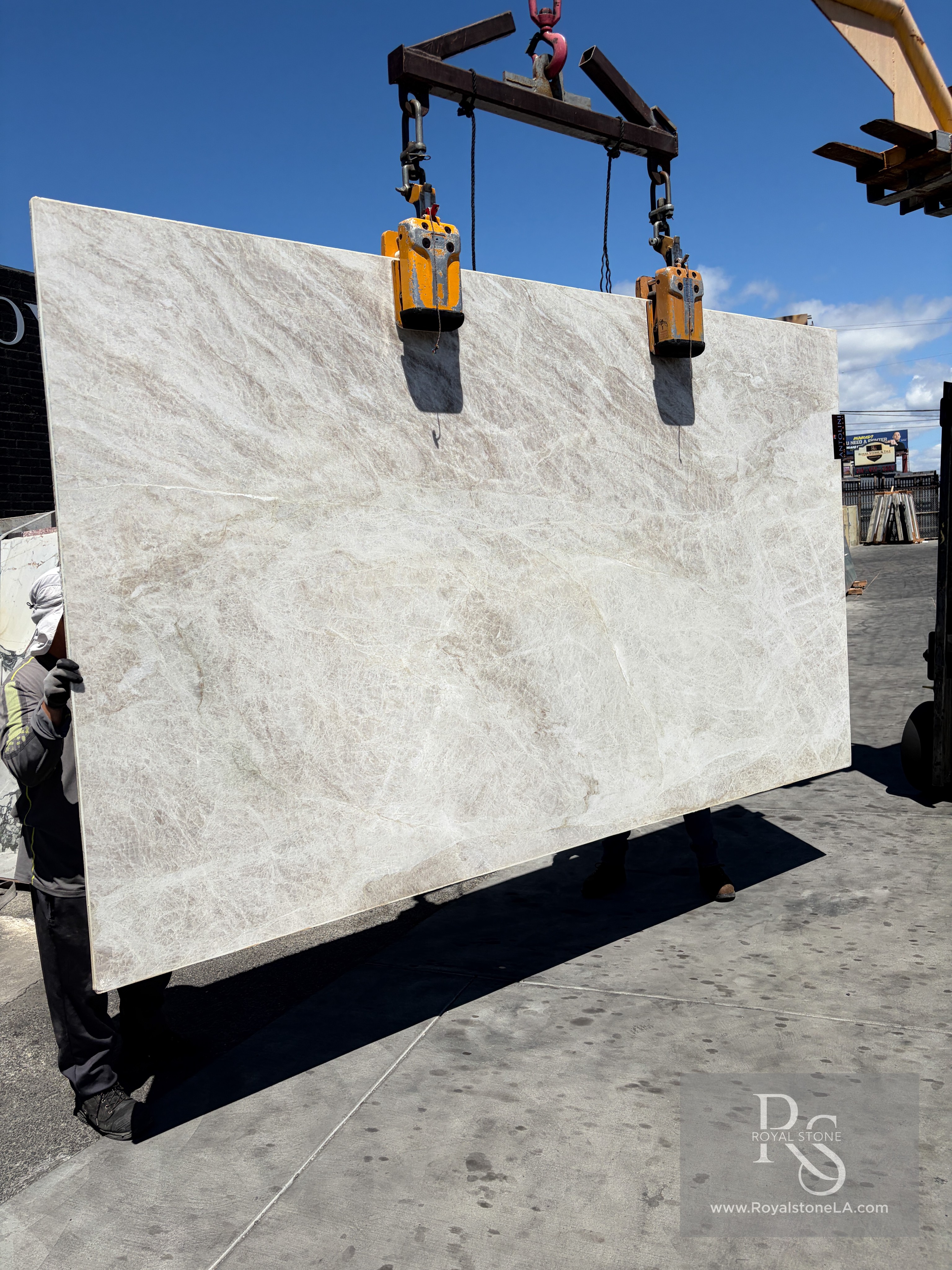 Antolini Taj Mahal Select Light Shade Quartzite slab in soft-leather finish lifted on the crane against blue sky, pale ivory and oyster cream with quiet tan drift