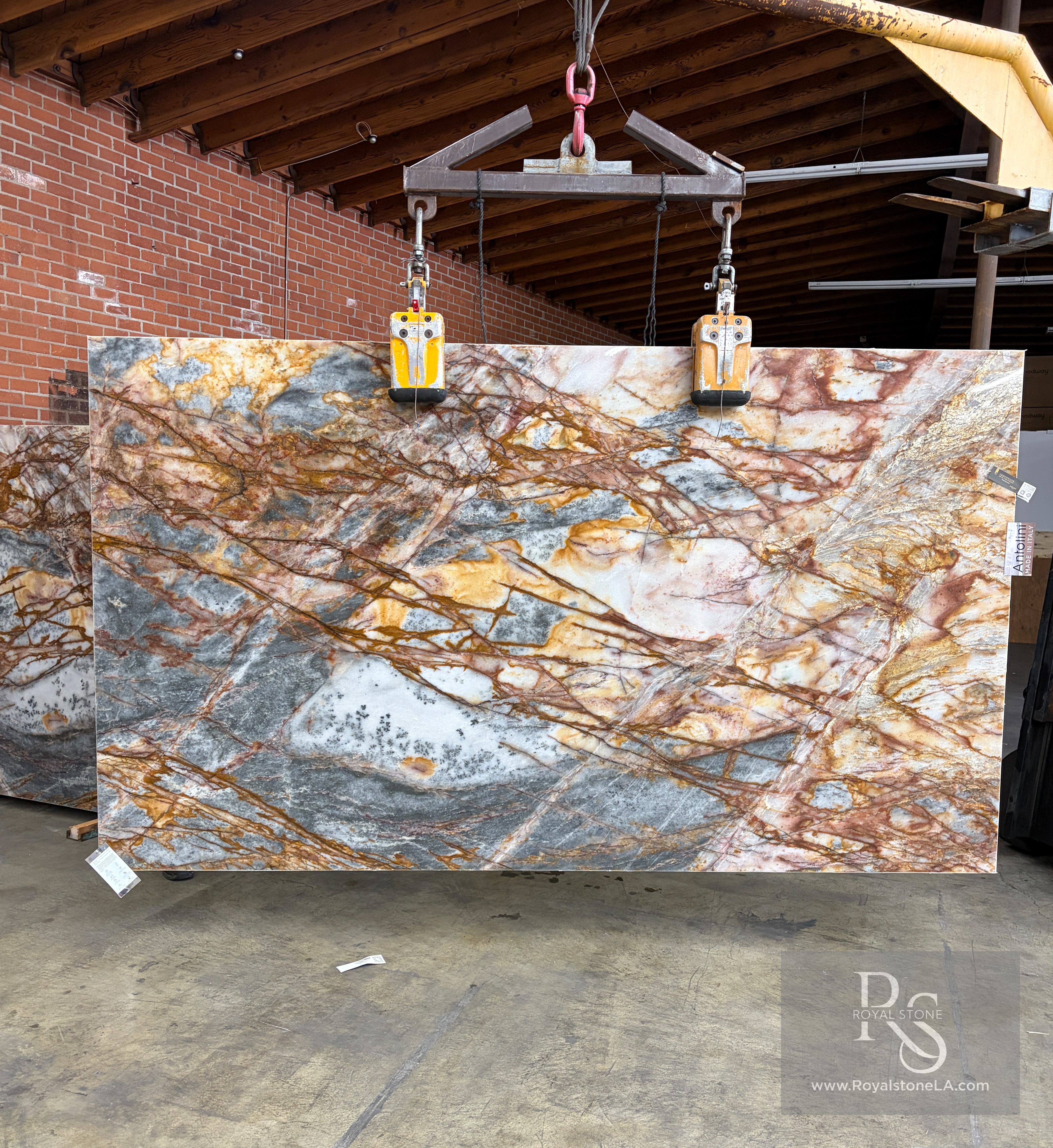 Antolini Cristallo Etrusco quartzite slab, 2cm polished, 78 by 136 inches, with translucent crystal field crossed by copper and rust oxidized veining over cool gray clouds, hanging from a crane at the Royal Stone Los Angeles yard